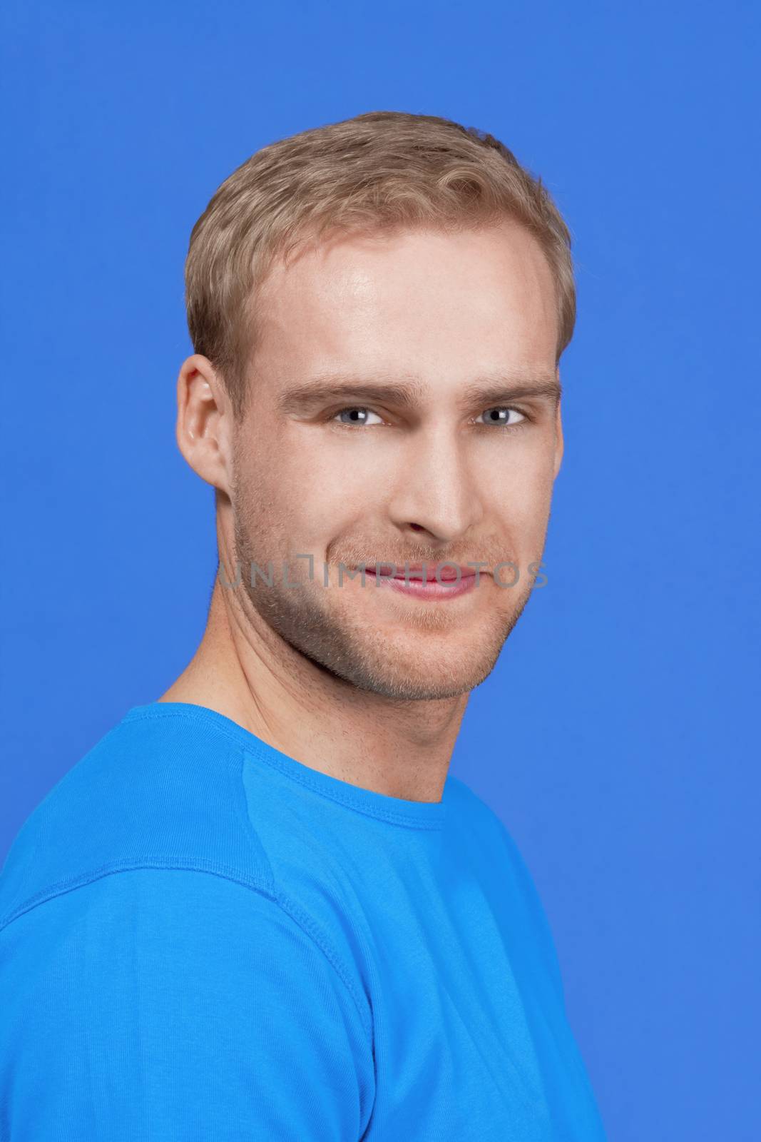 portrait of a young man with blond hair smiling - isolated on blue