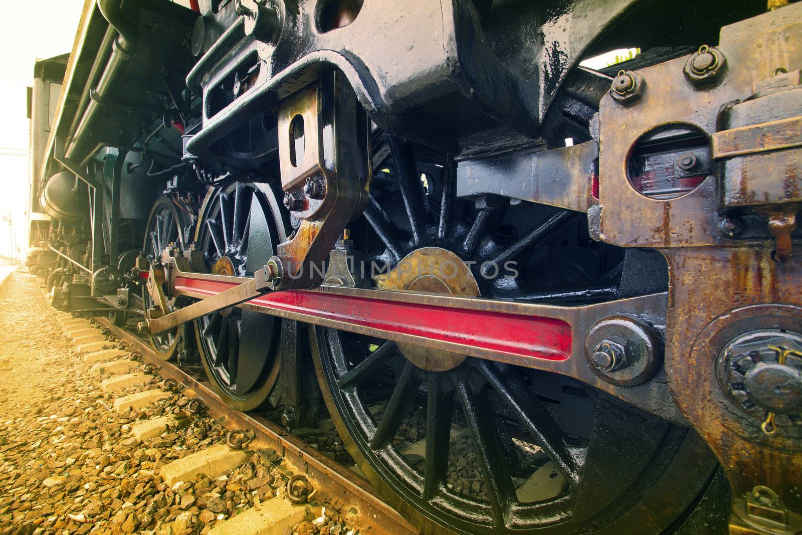 iron wheels of stream engine locomotive train on railways track perspective to golden light forward use for old and classic period land transport and retro vintage style background 