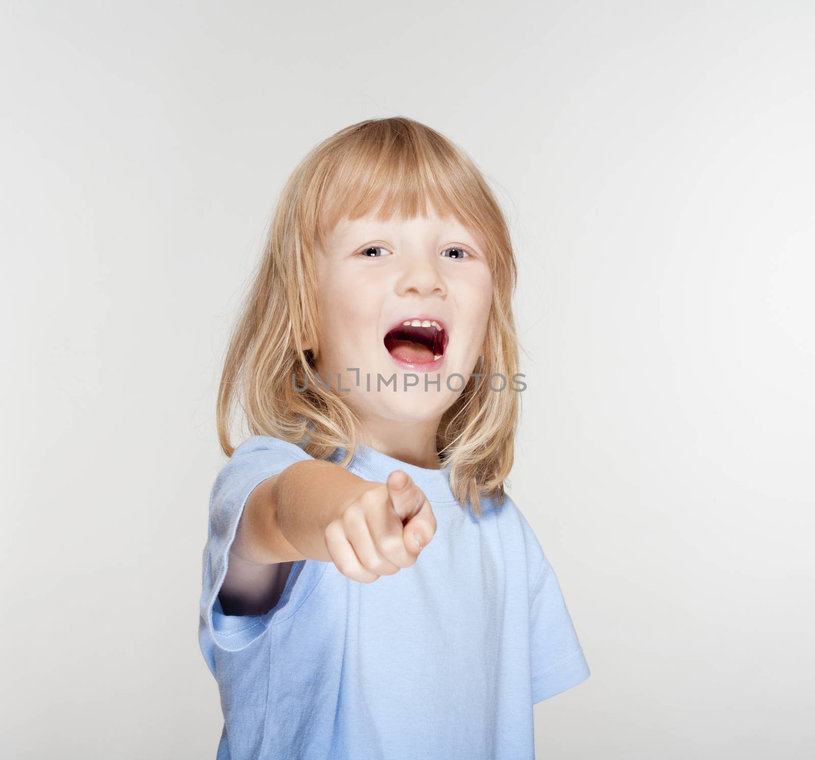 boy with long blond hair pointing towards the camera - isolated on gray