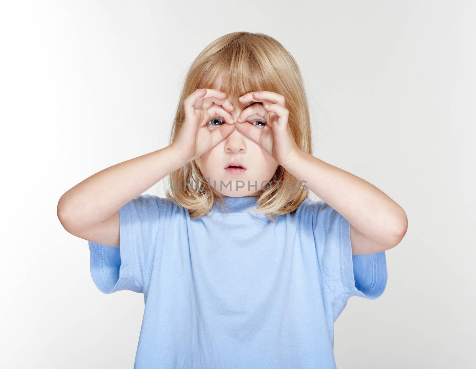 boy with long blond hair looking through fingers as binaculars - isolated on gray