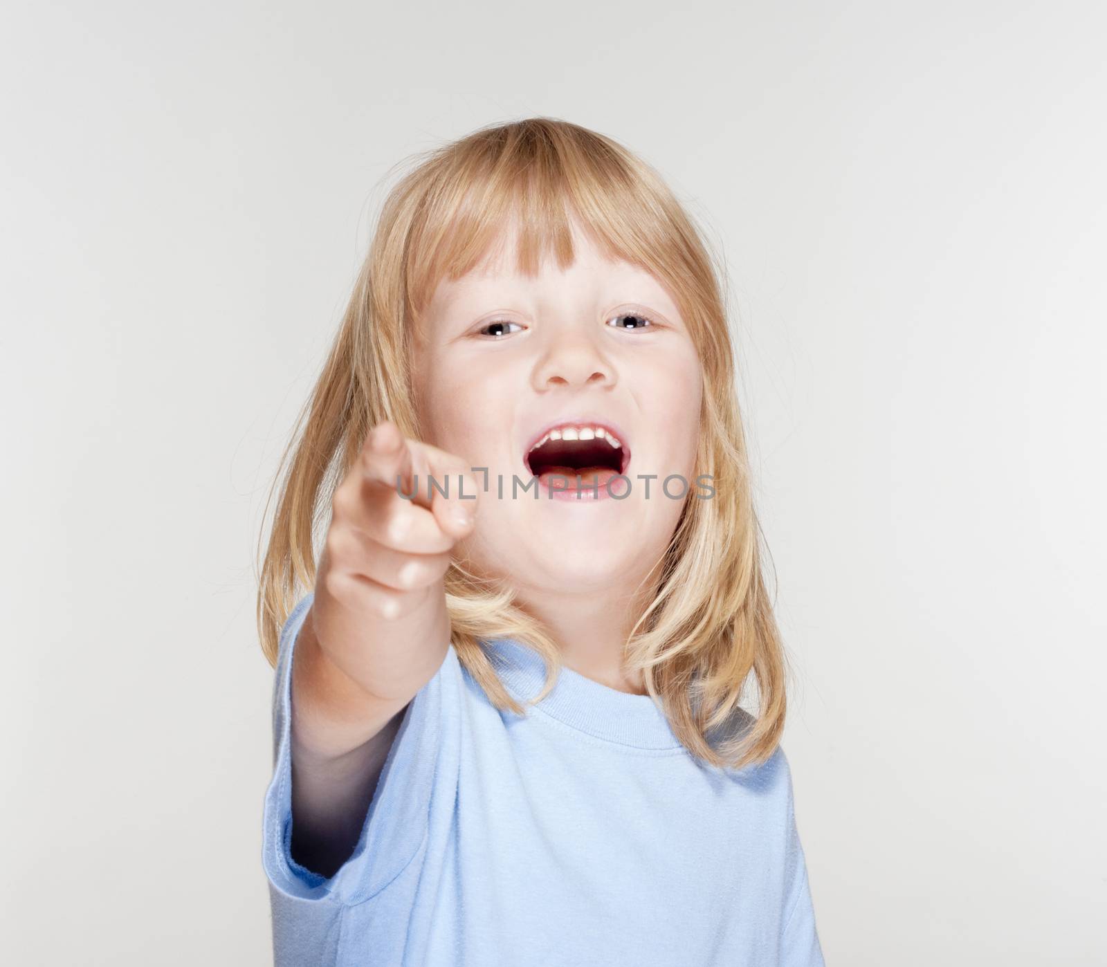 boy with long blond hair pointing towards the camera - isolated on gray