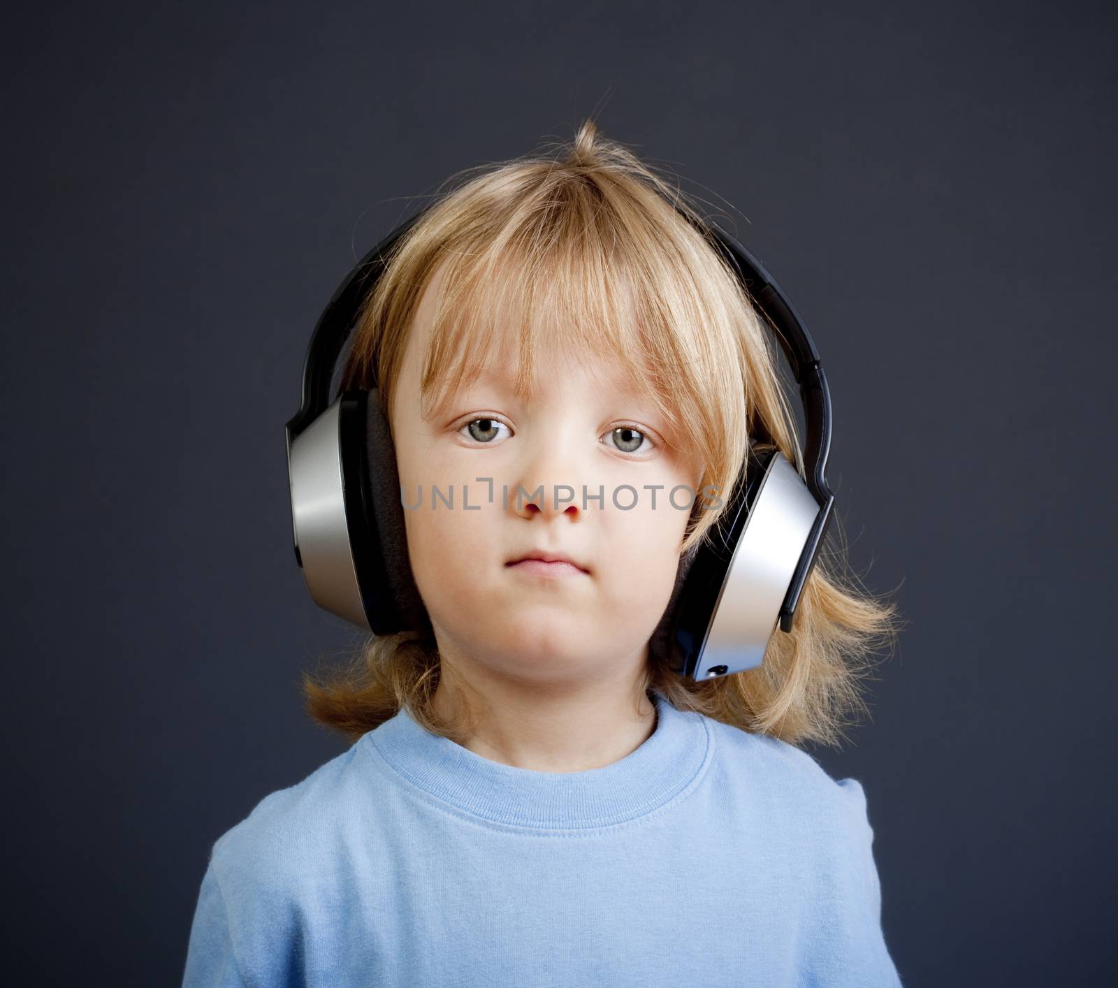 boy with long blond hair listening to music in headphones - isolated on dark blue