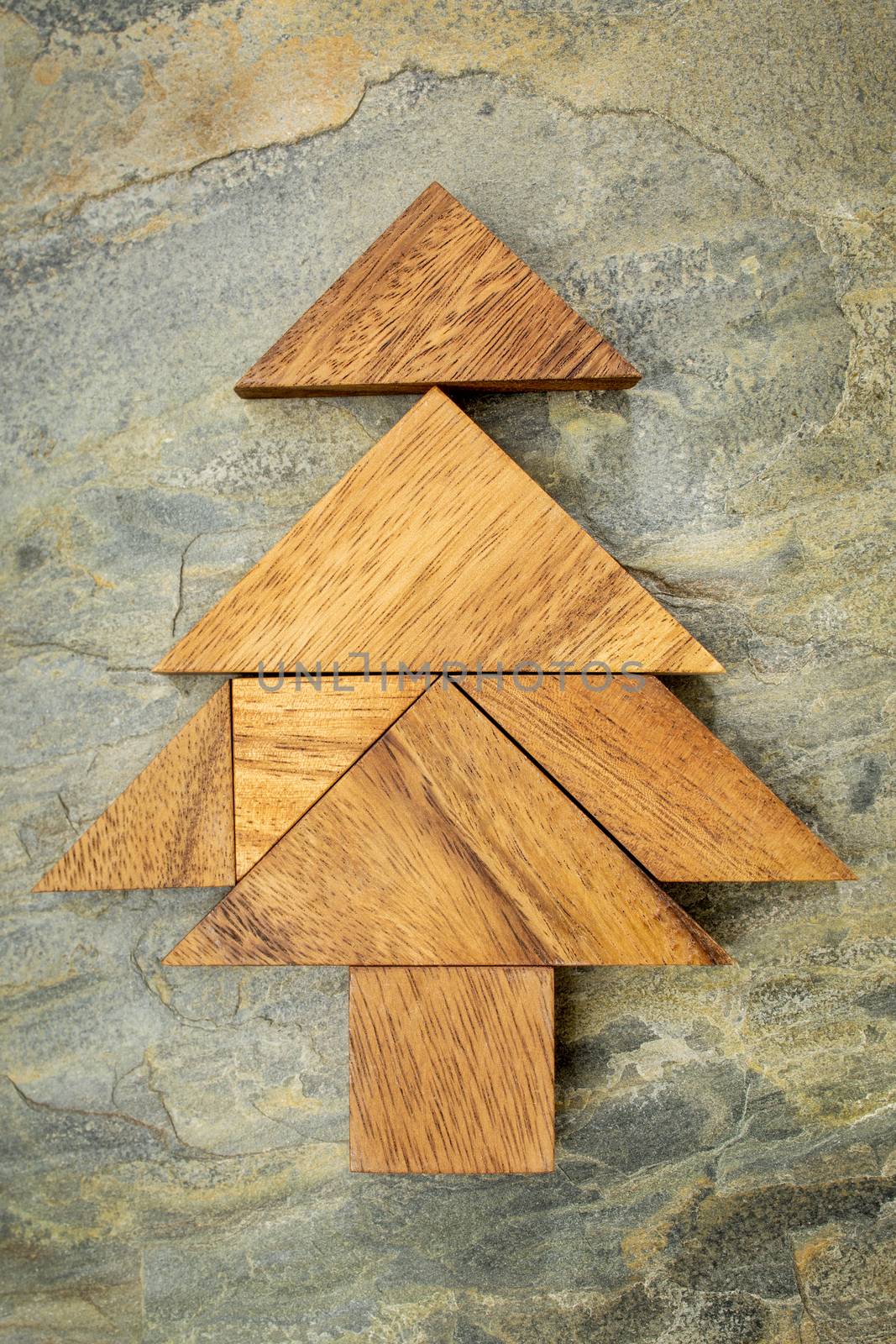 abstract picture of a Christmas tree built from seven tangram wooden pieces over a slate rock background, Christmas holiday concept, artwork created by the photographer