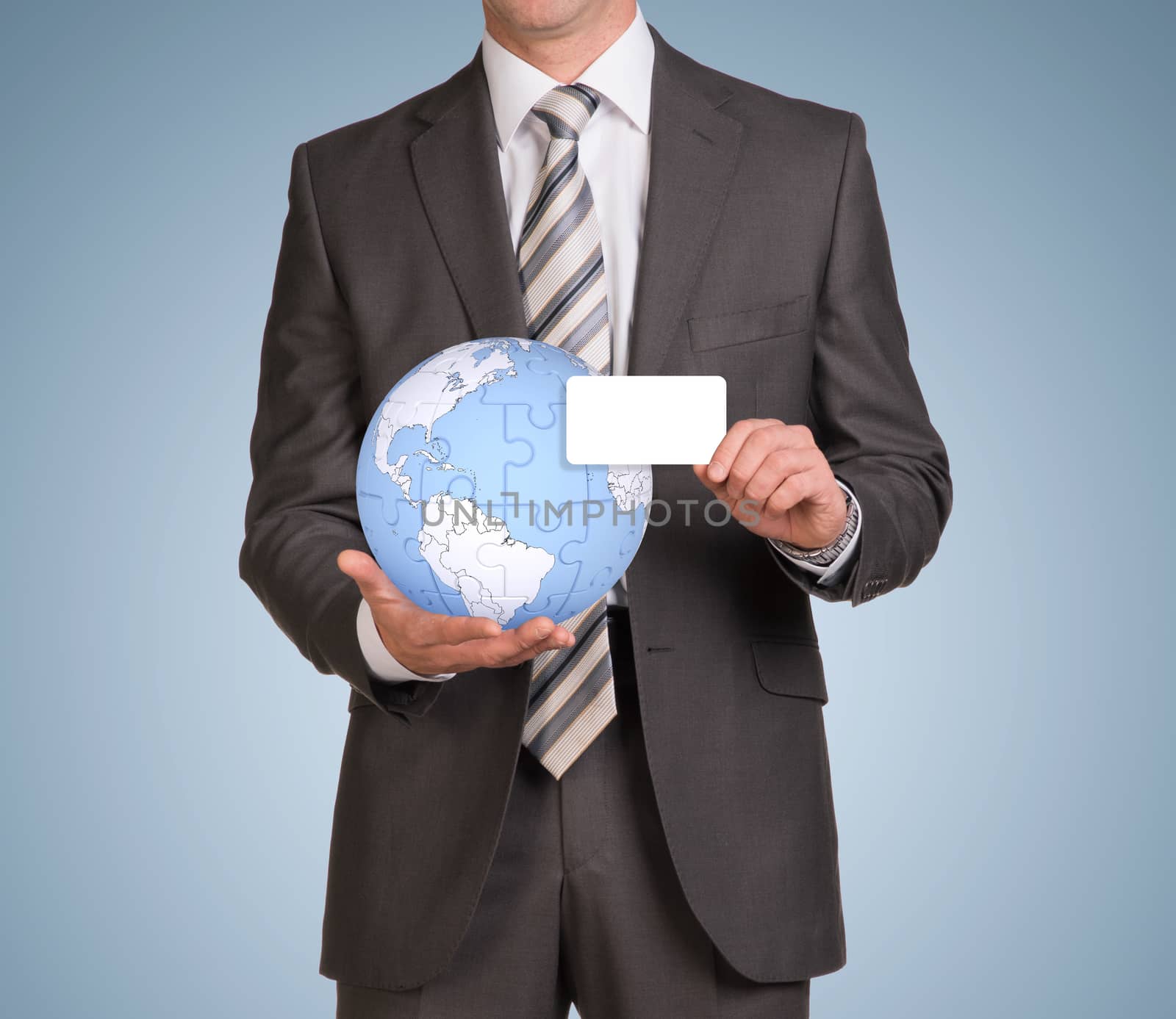 Businessman in suit hold empty card and earth globe consisting of puzzles. Blue background