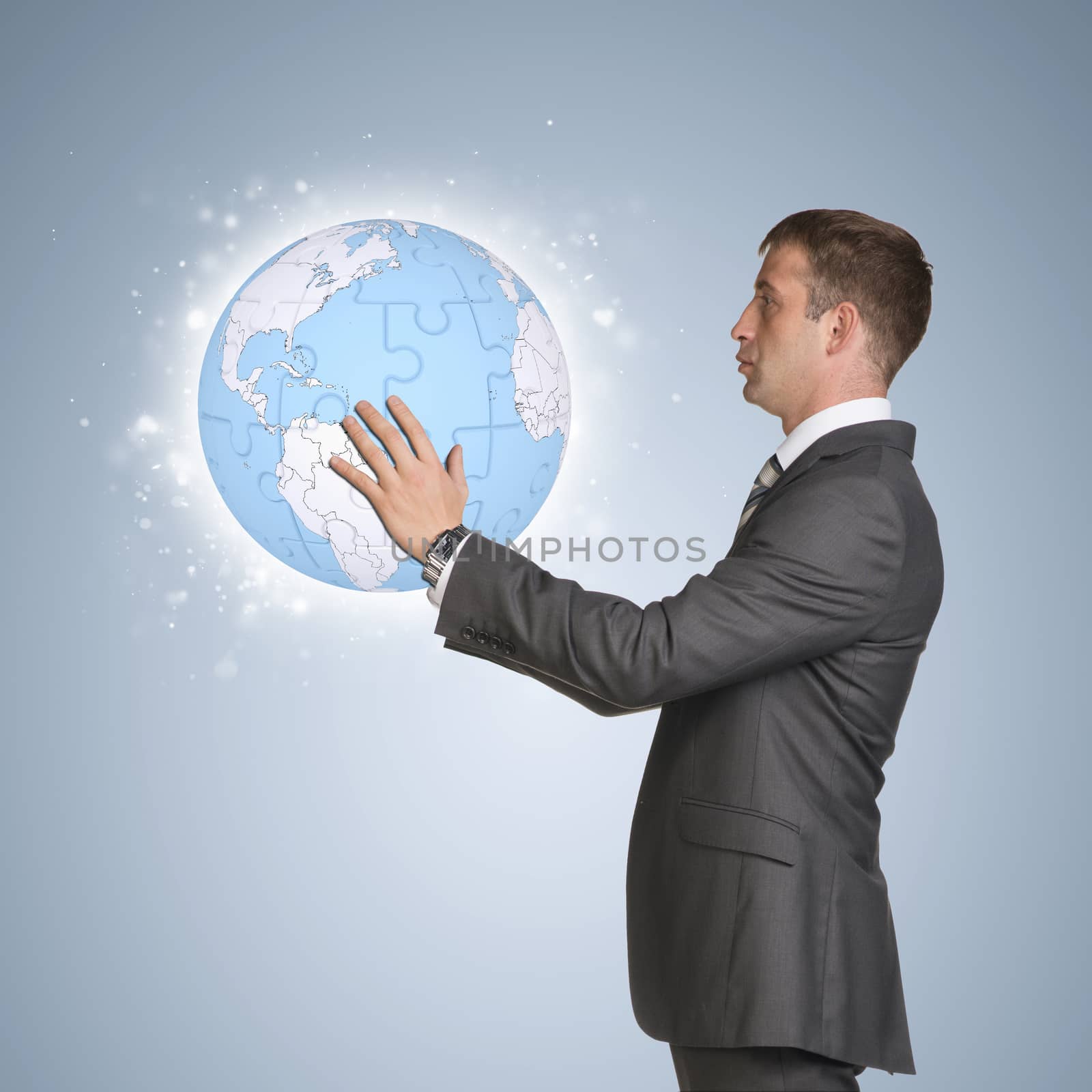 Businessman in suit hold earth globe consisting of puzzles by cherezoff