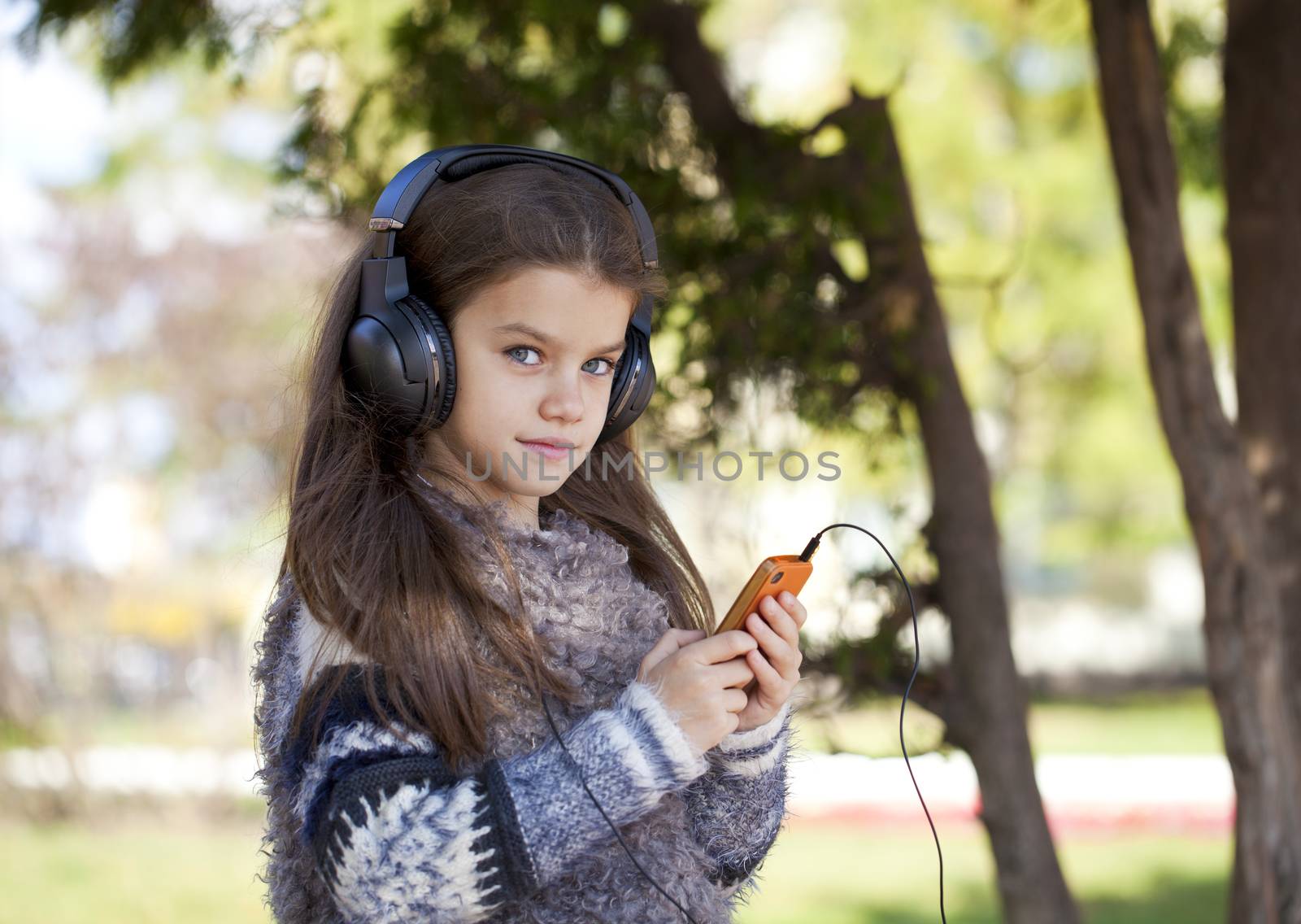 Beautiful little girl listening to music on headphones in autumn park