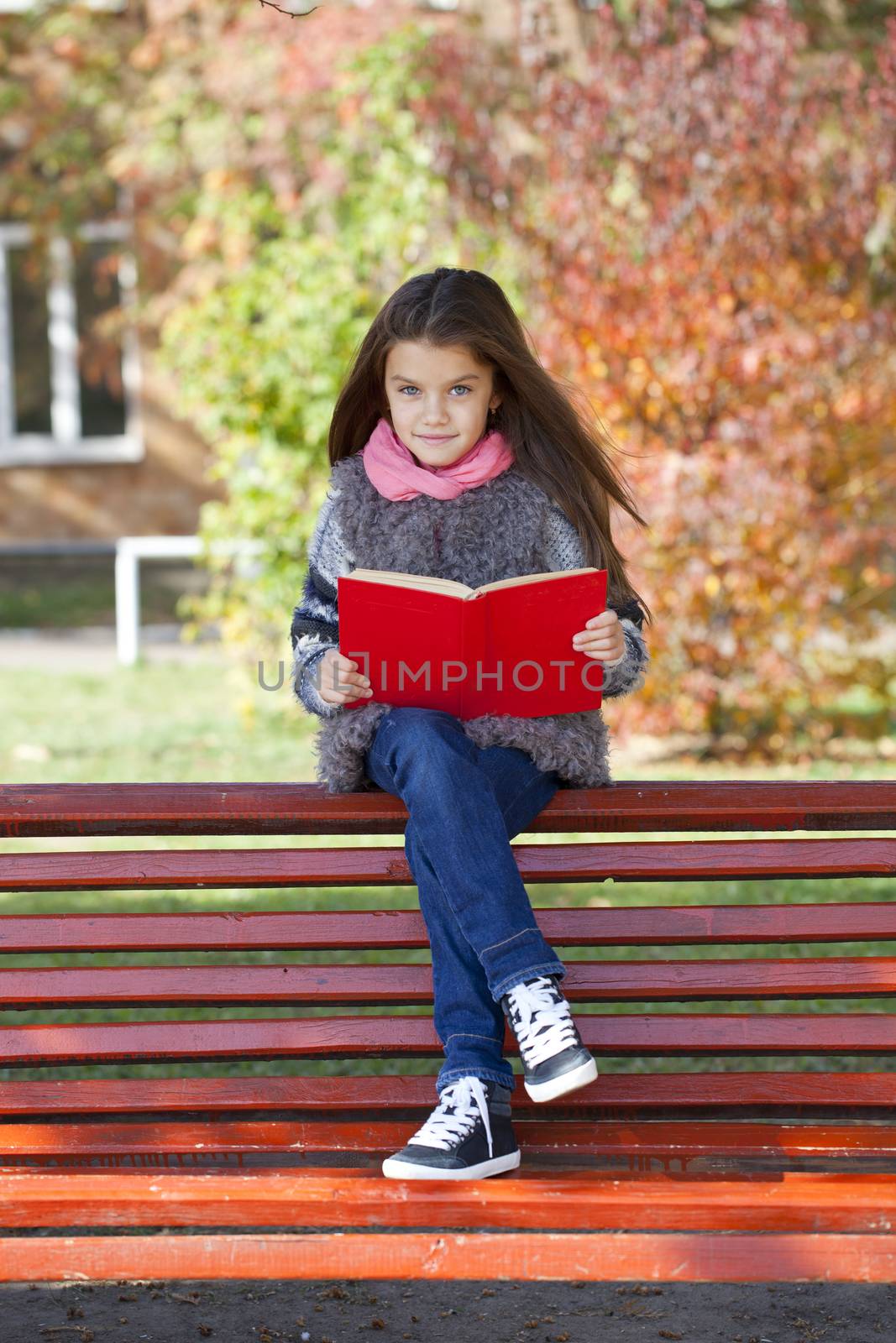 Beautiful little girl sitting on a bench in autumn park