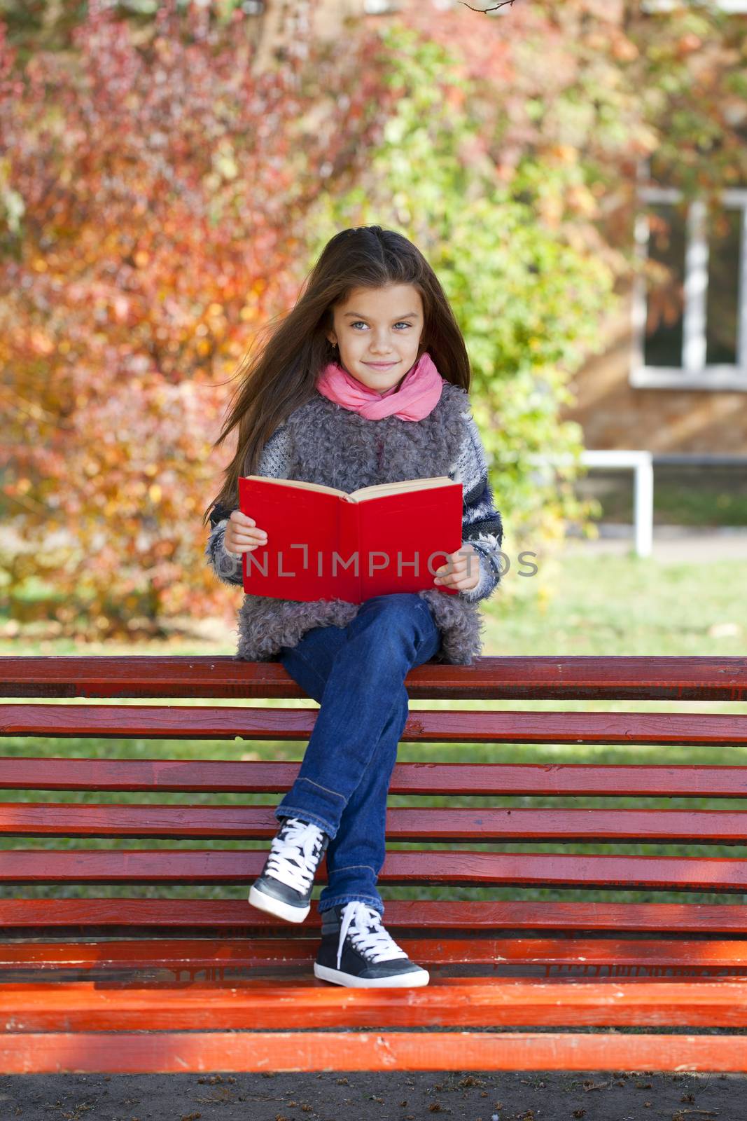 Beautiful little girl sitting on a bench in autumn park