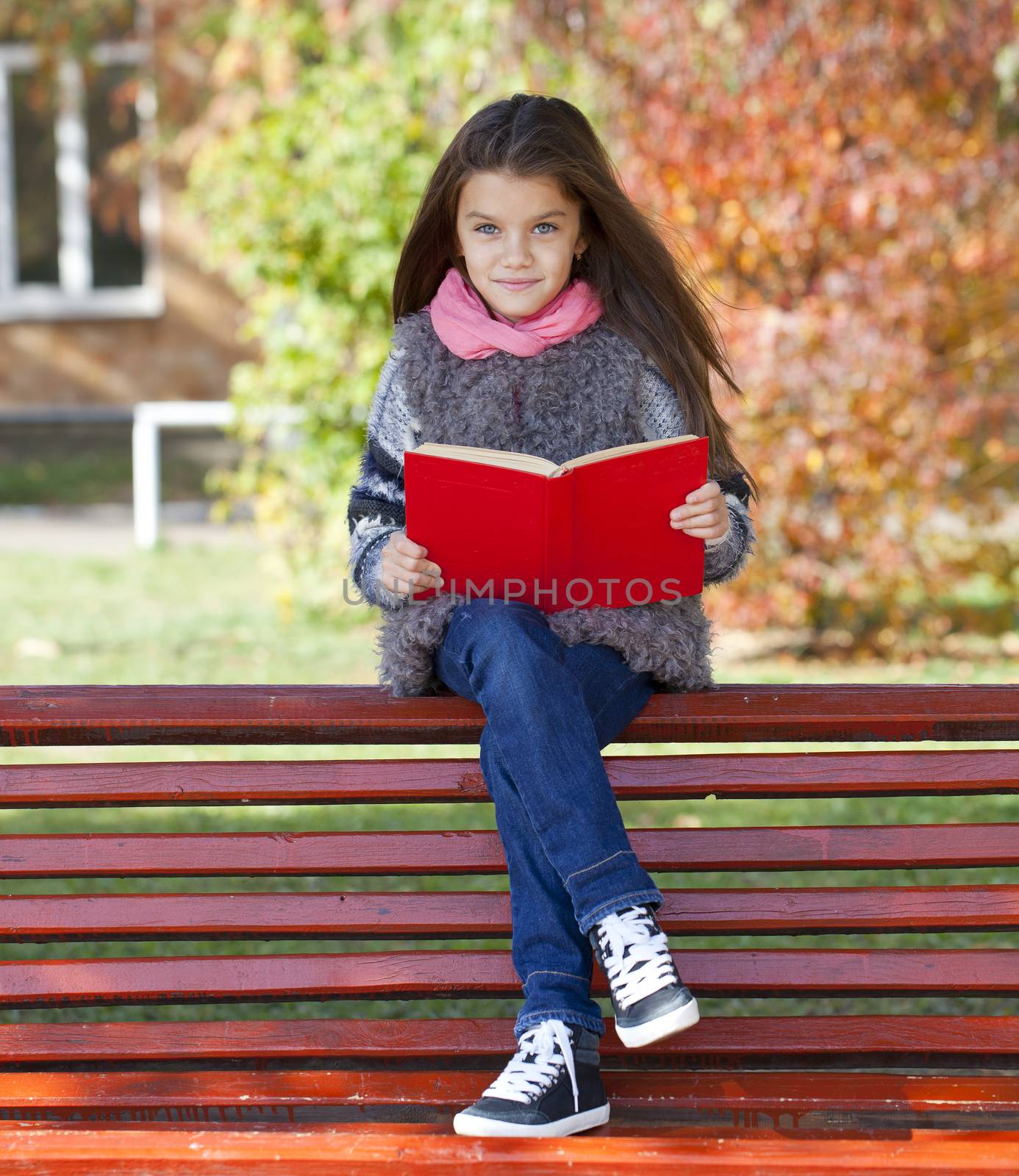 Beautiful little girl sitting on a bench in autumn park