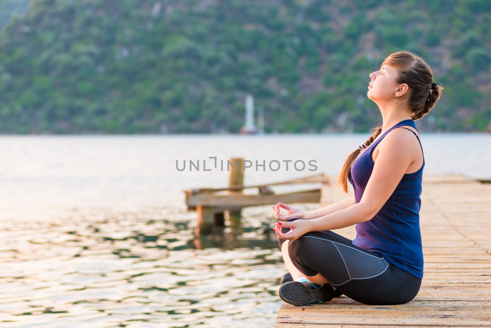 girl with a long braid relaxes in a lotus position on the pier by kosmsos111