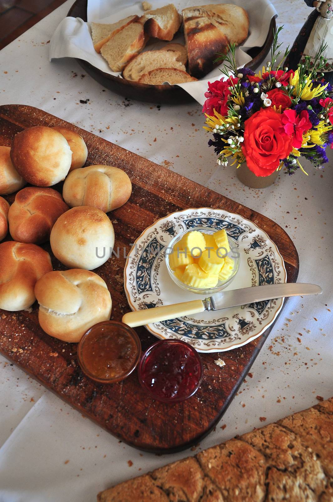 Freshly baked white buns laid out on cutting board with butter buttons and jam for breakfast table in the hospitality industry or home bake industry.