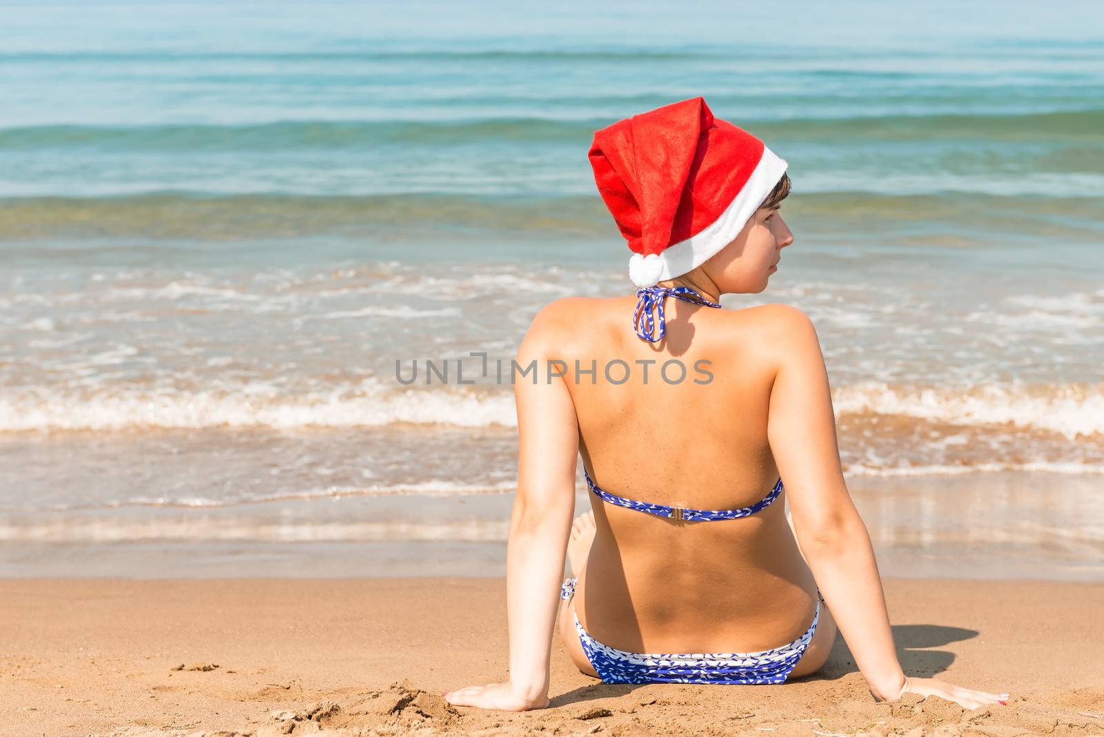 young girl in a Christmas hat on the sand