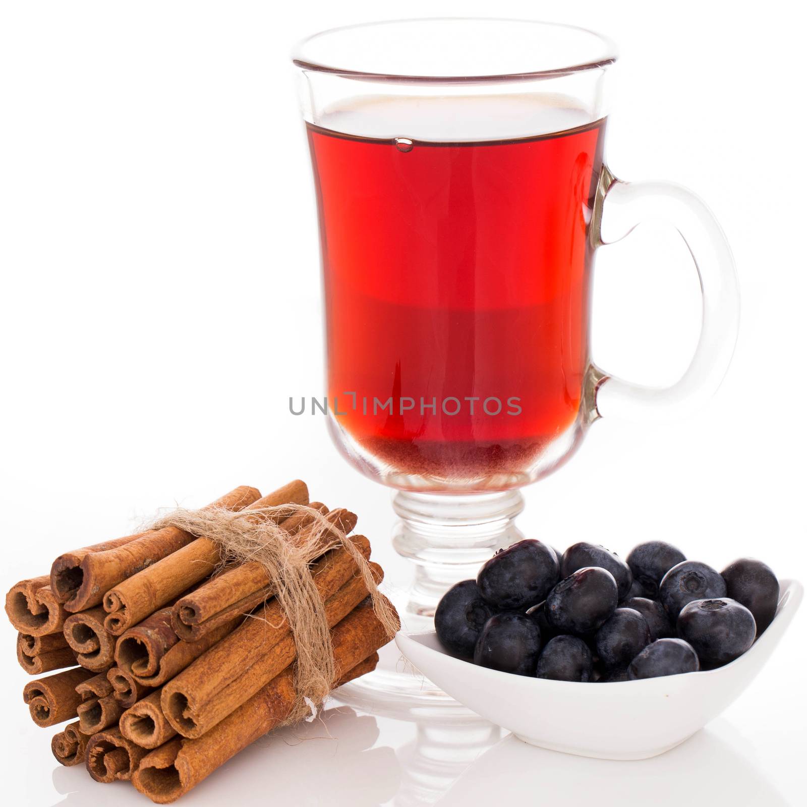 Glass of tea a stack of cinnamon and a plate with blueberries over a white background