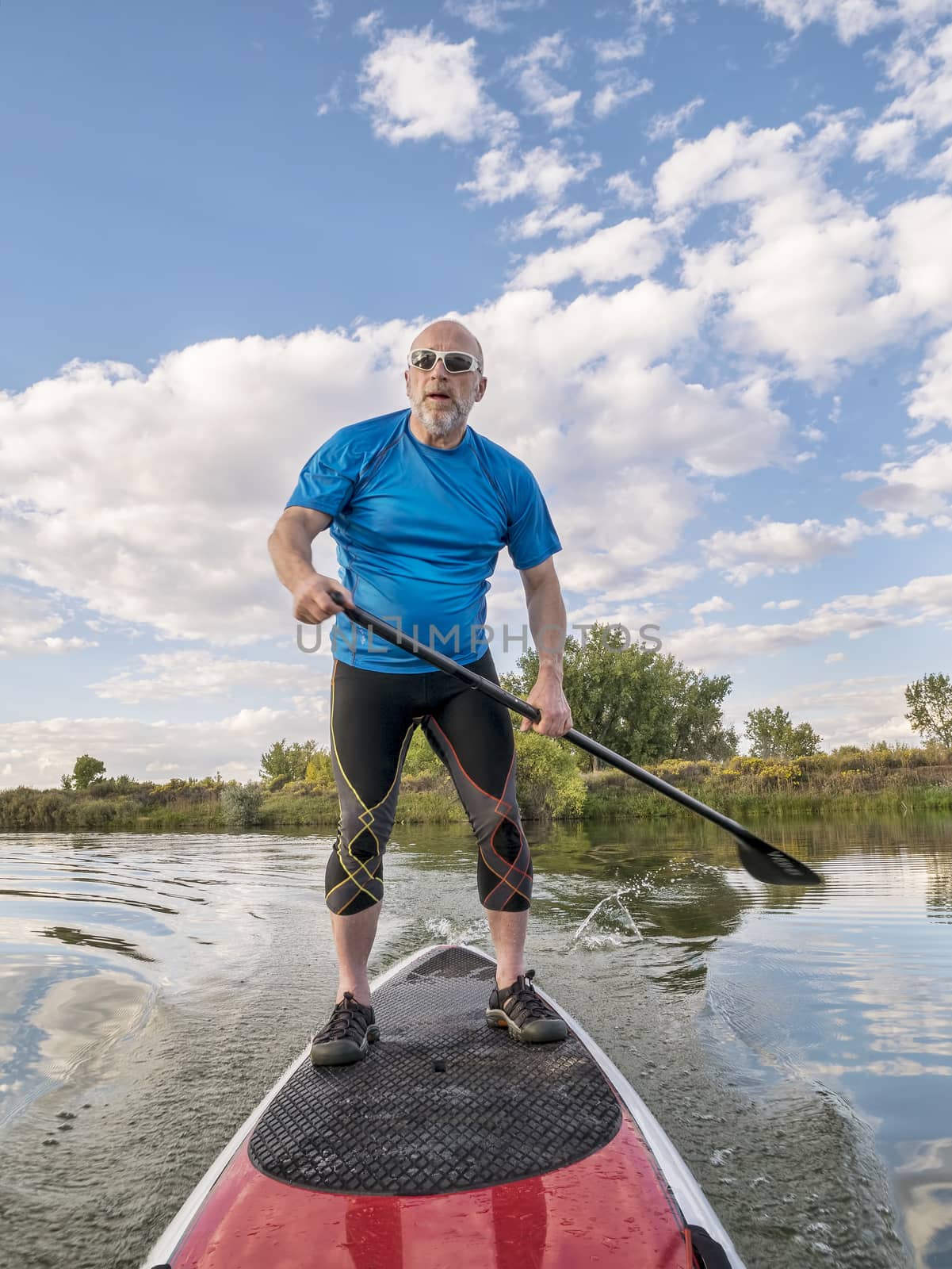 senior male paddler paddling a stand up paddleboard (SUP), calm lake in Colorado, late summer