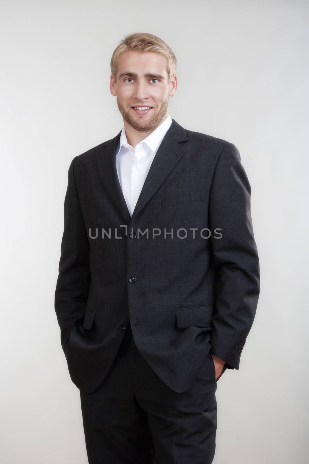 portrait of a young businessman with blond hair in suit standing - isolated on light gray