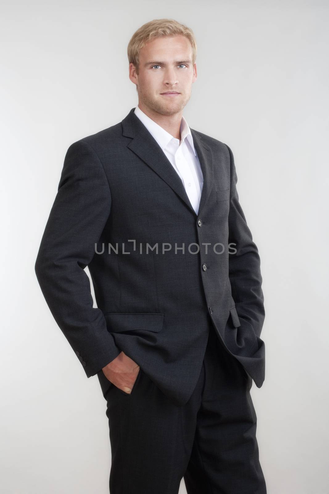 portrait of a young businessman with blond hair in suit standing - isolated on light gray