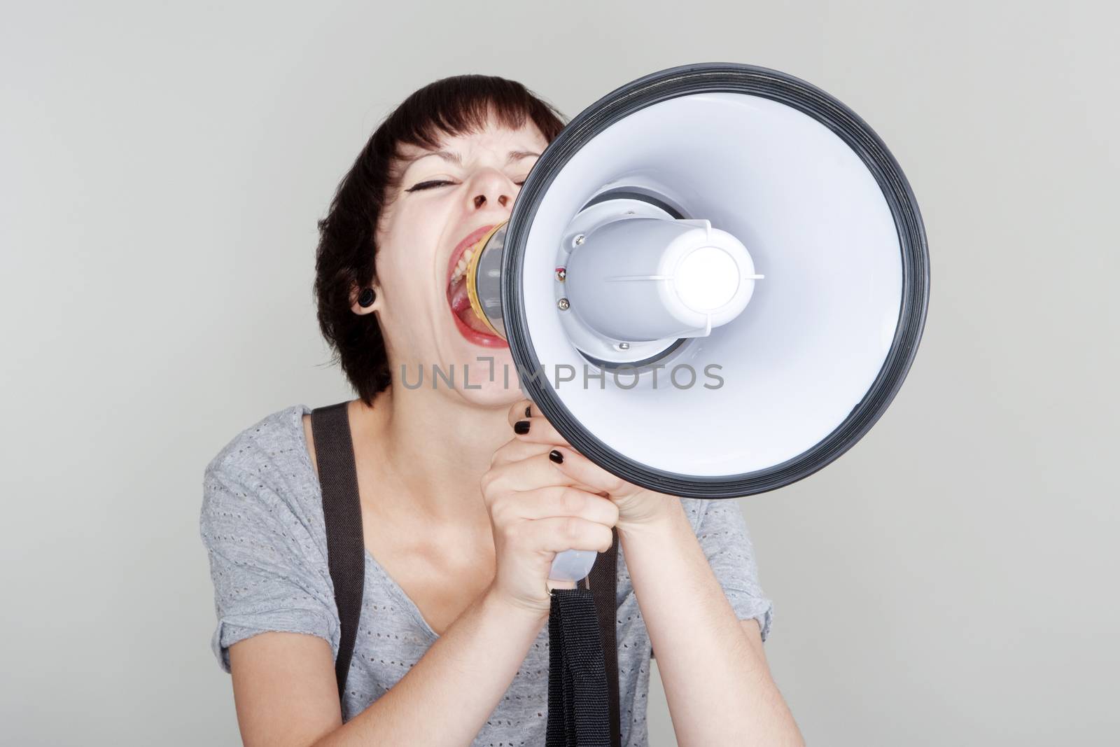 angry teenage girl yelling into a megaphone - isolated on gray