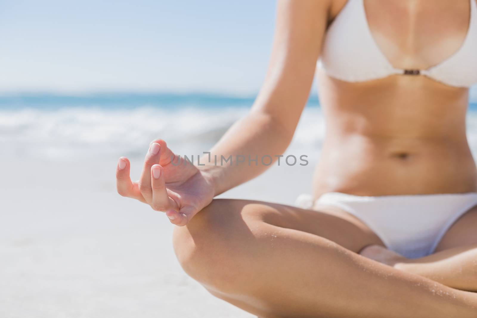 Girl in white bikini sitting in lotus pose on beach by Wavebreakmedia