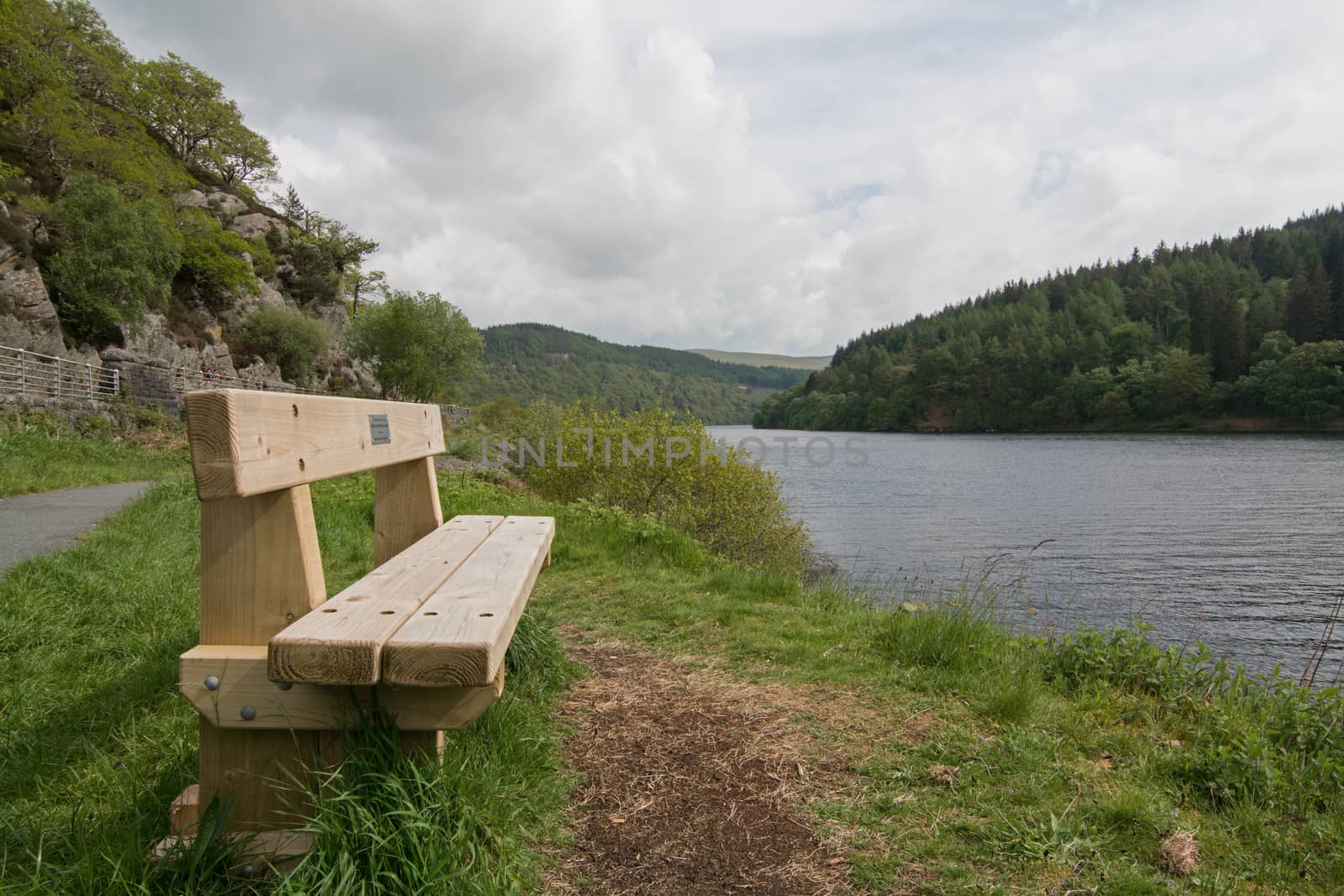 A wooden bench, set beside a picturesque lake, with wooded hills in the background