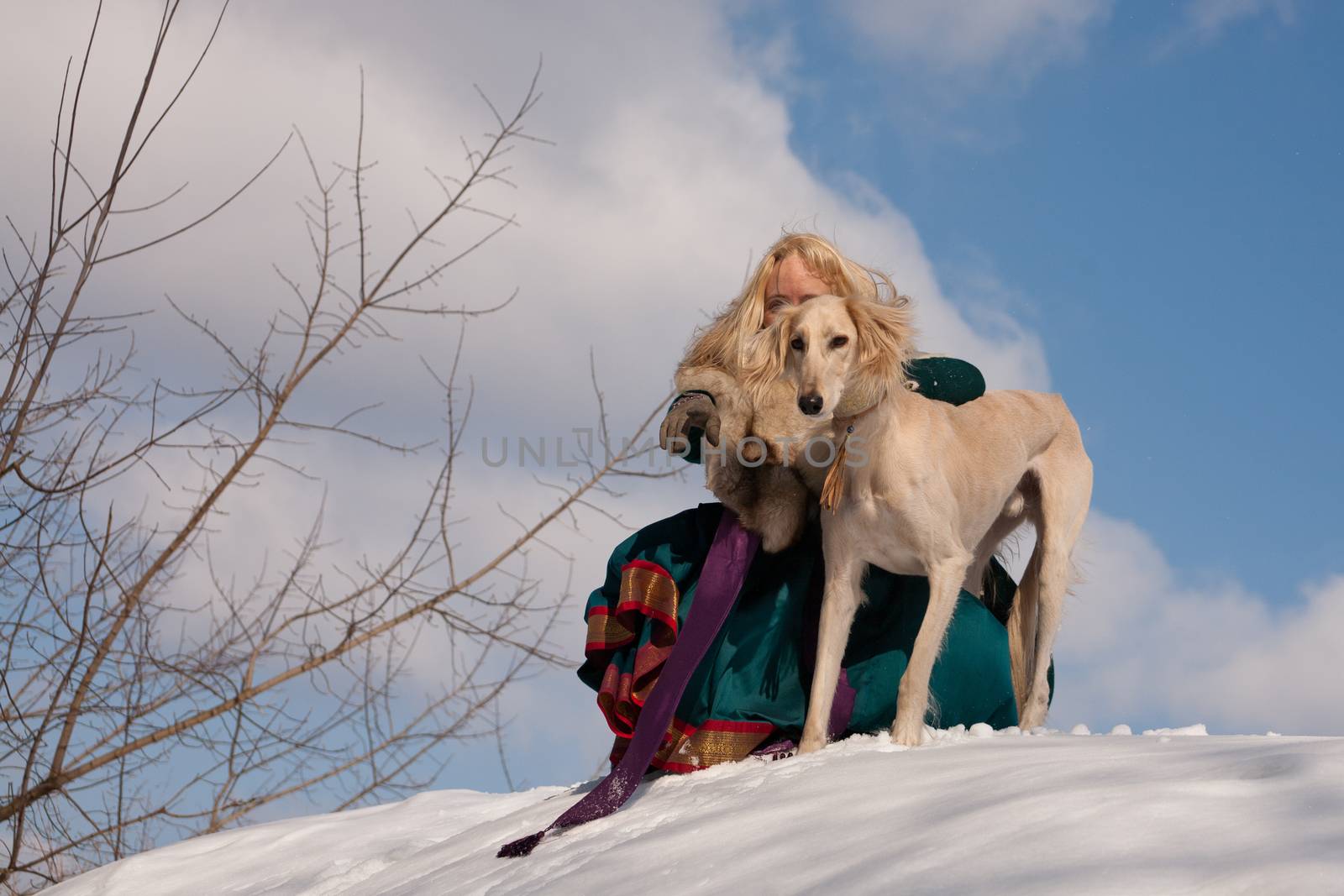 A blonde girl and a white saluki on snow
