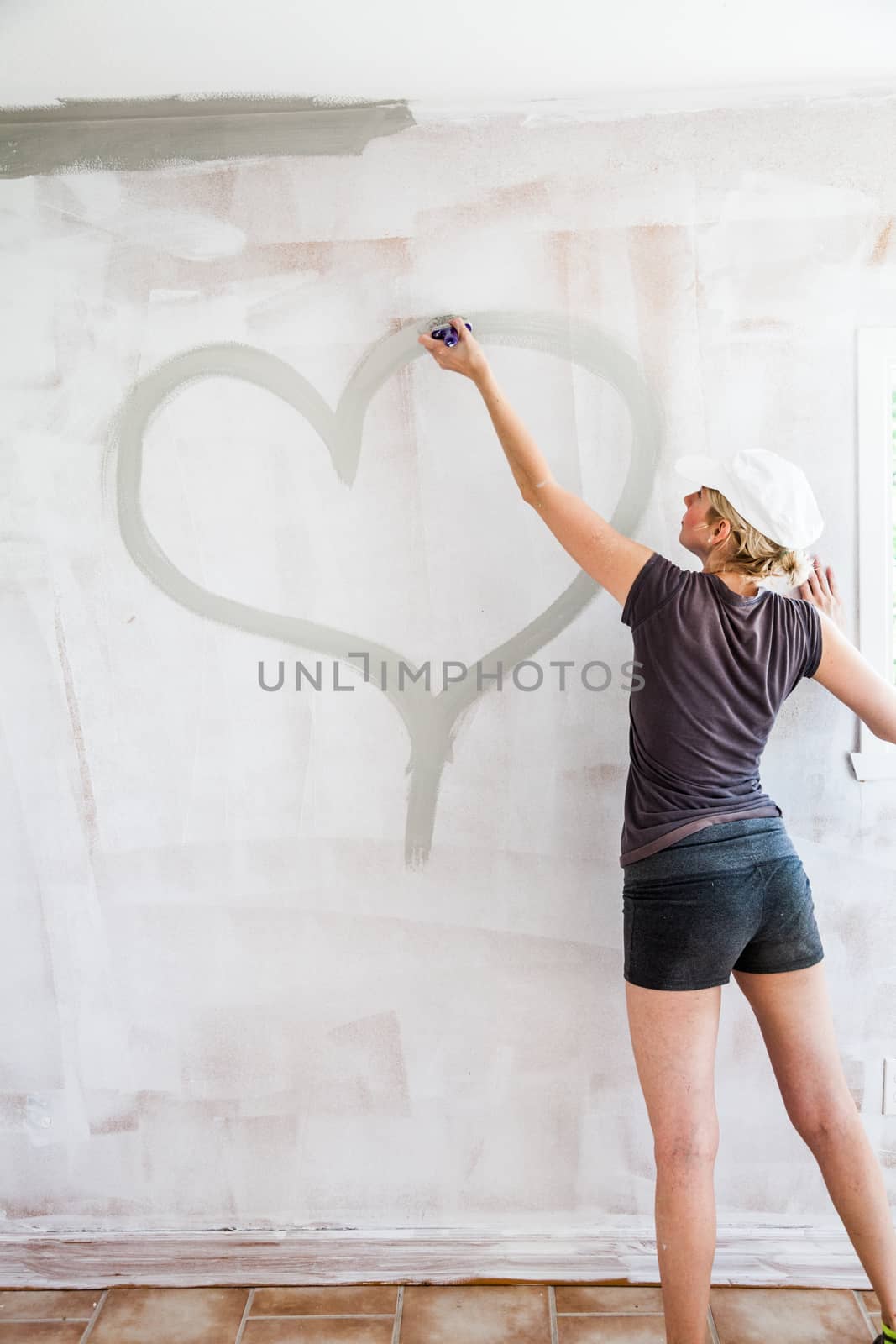 Woman Sketching a Hearth Directly on the Wall with Gray Paint - Love Concept