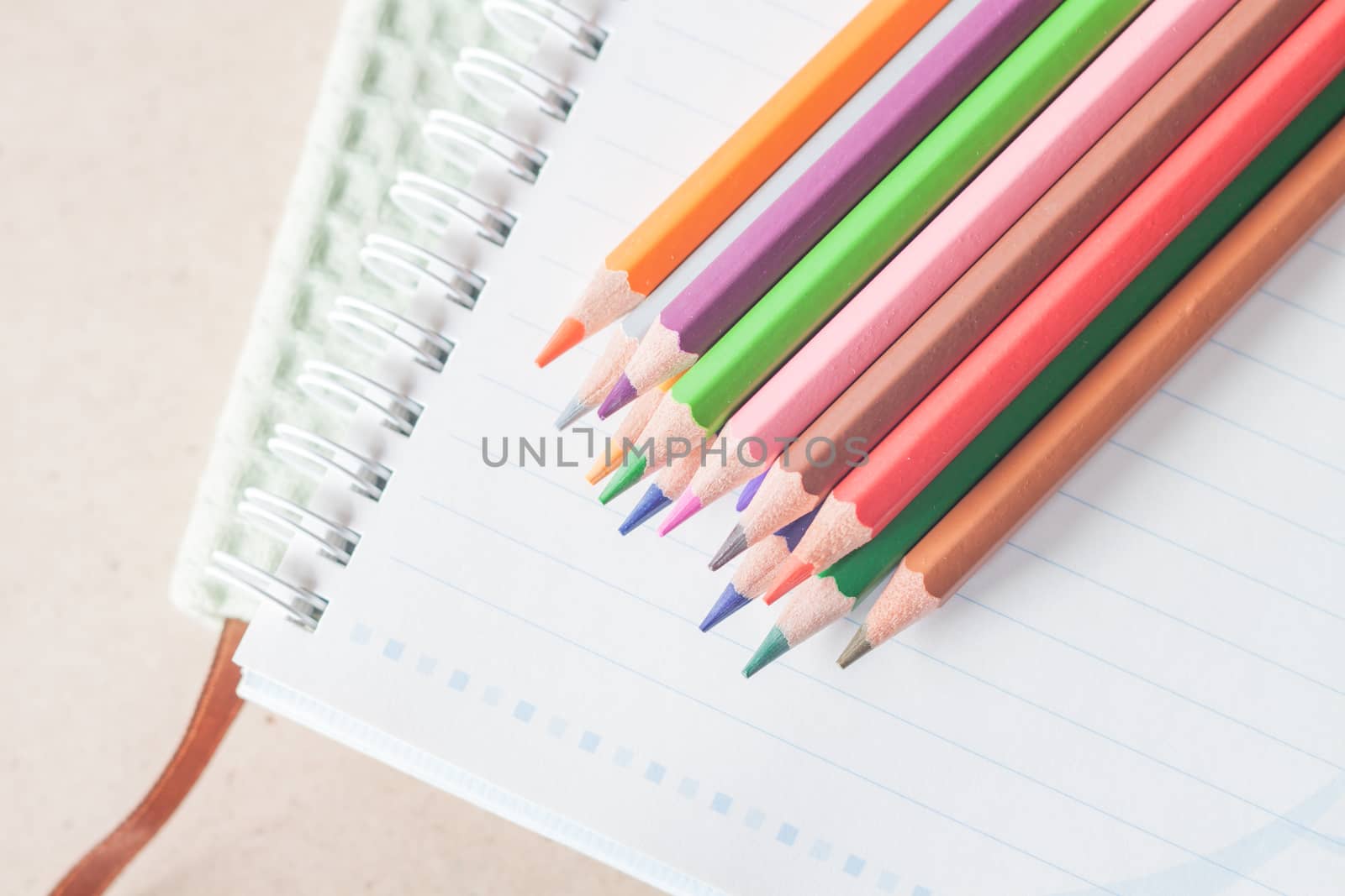 Top view of colorful pencil crayons on spiral notebook and green by punsayaporn