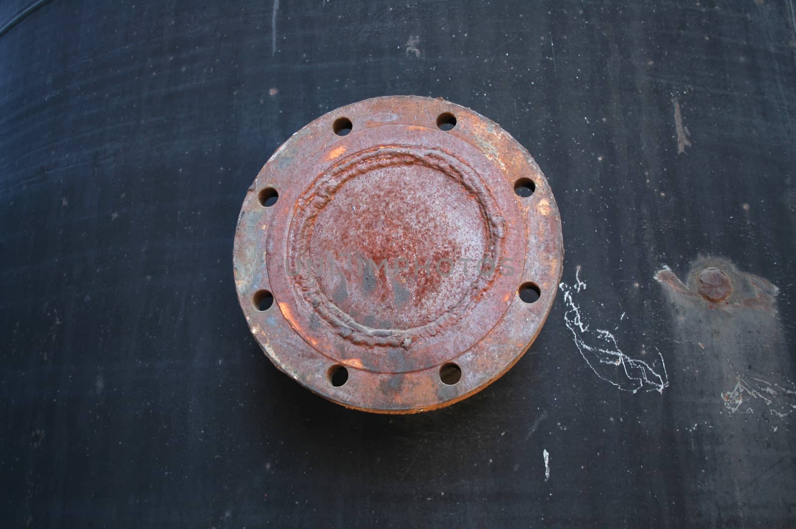 A rusted, reddish release valve with a circle of open holes all round on a dark, charcoal background.
