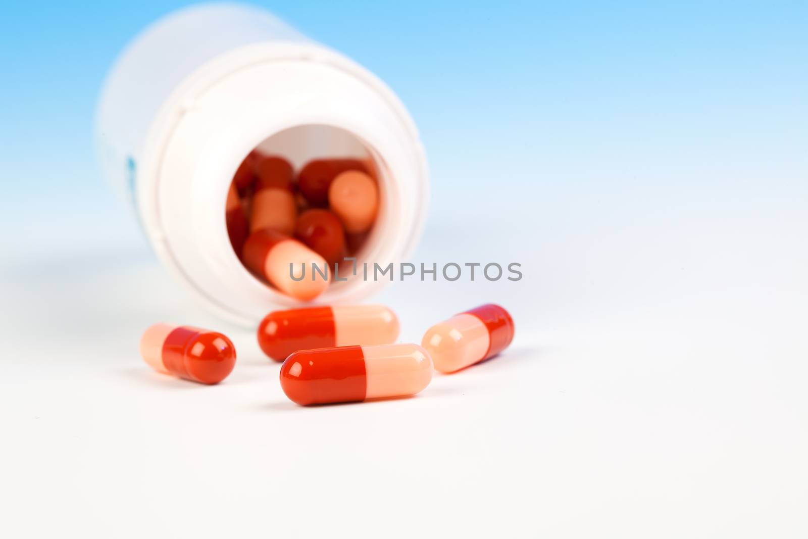 Pills spilling out of pill bottle isolated on blue (with sample text)