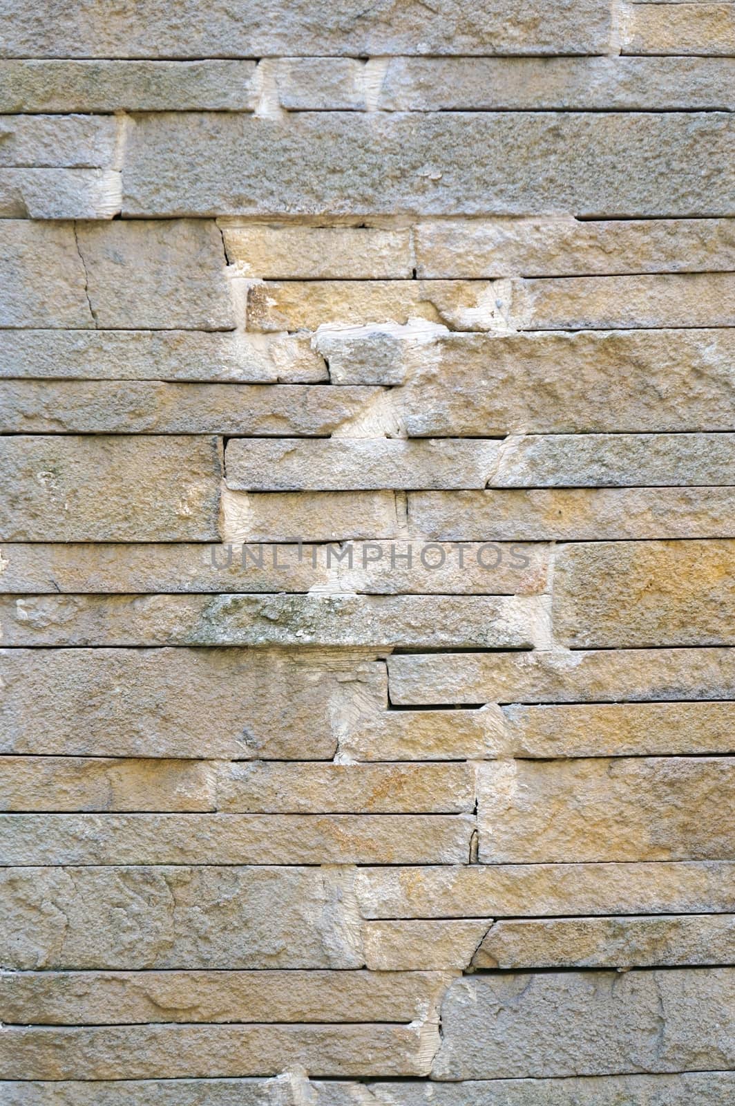 A fence made of beige narrow stones fastened by cement as background