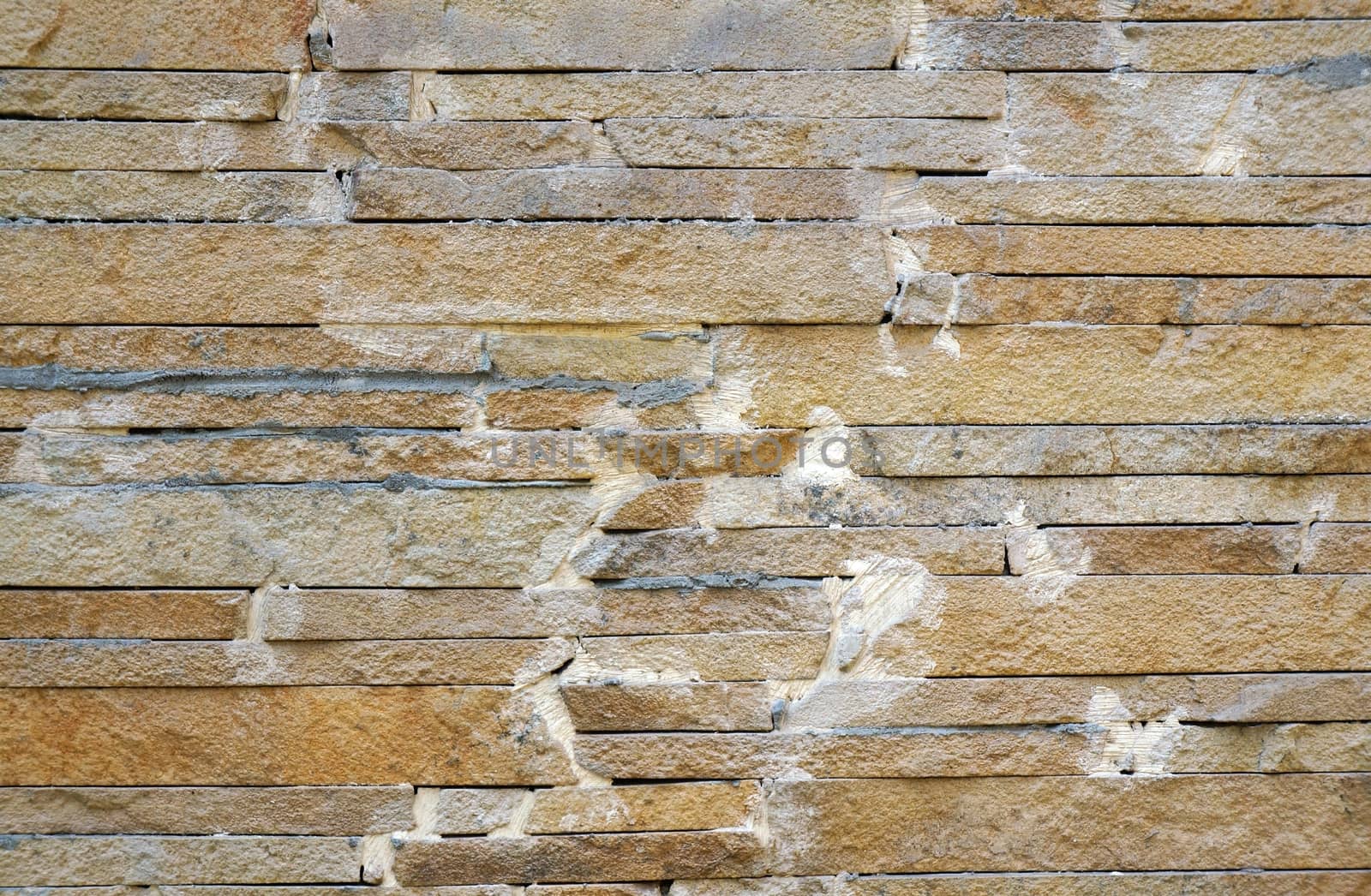 A fence made of beige narrow stones fastened by cement as background                               