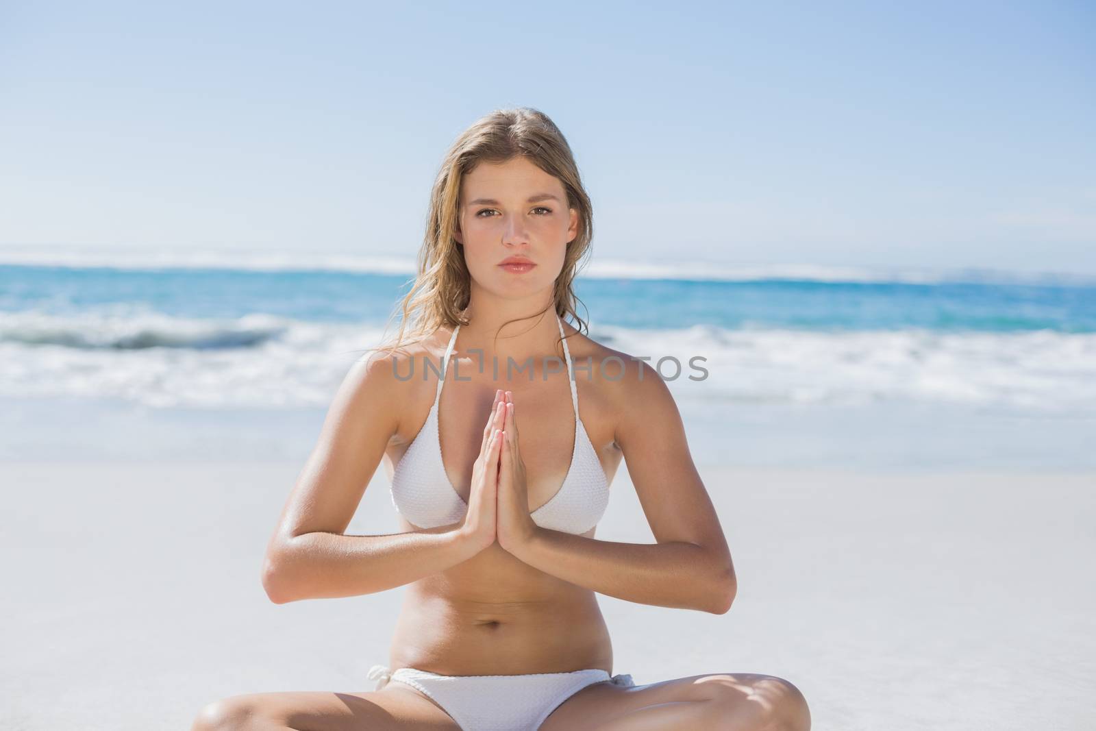 Beautiful girl in white bikini sitting in lotus pose on beach by Wavebreakmedia