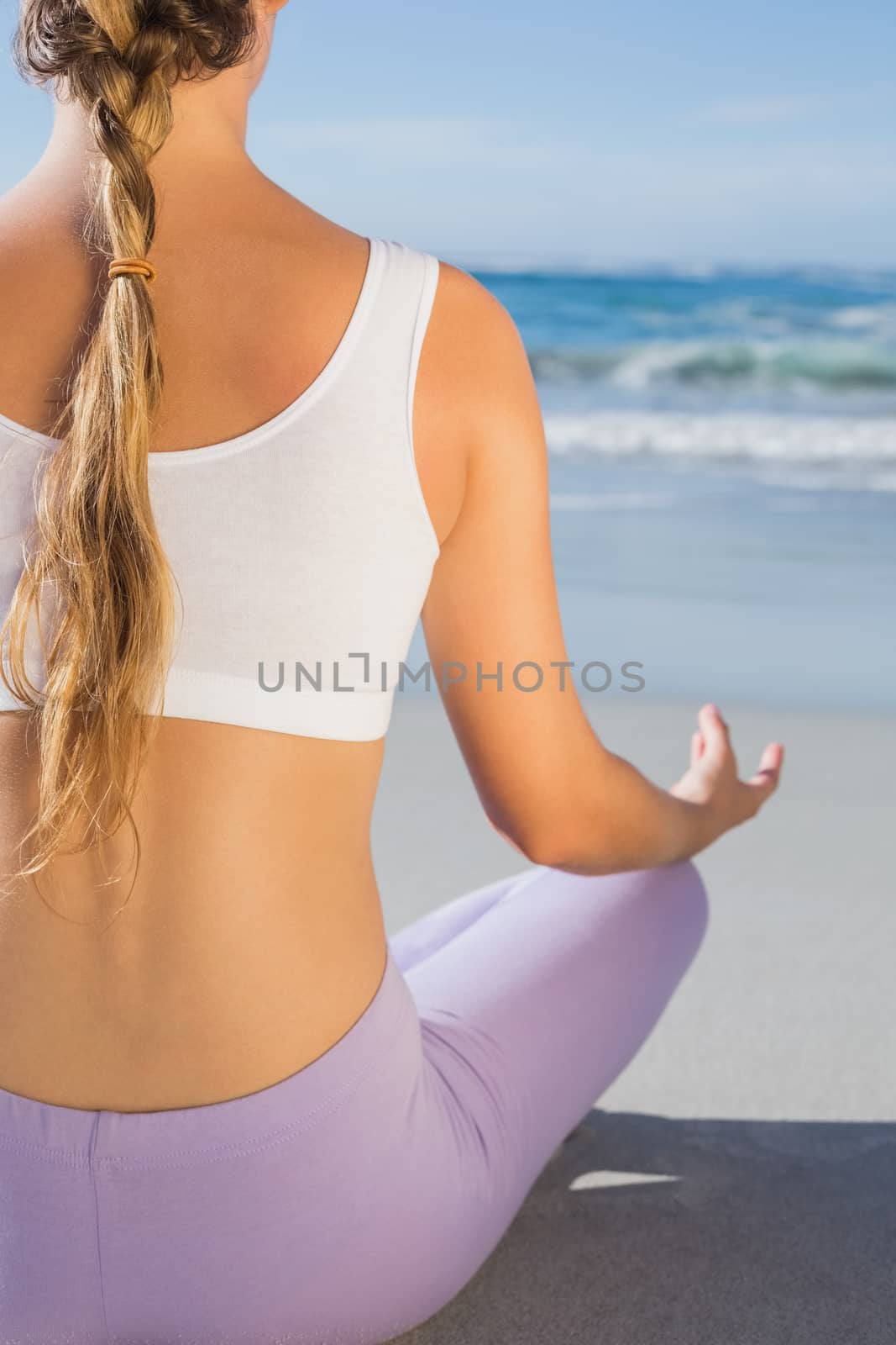 Sporty blonde sitting in lotus pose on the beach on a sunny day