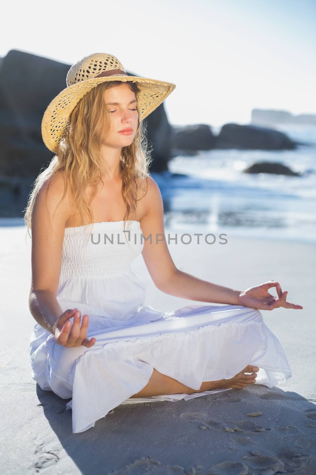 Beautiful blonde in sundress sitting in lotus pose on the beach by Wavebreakmedia