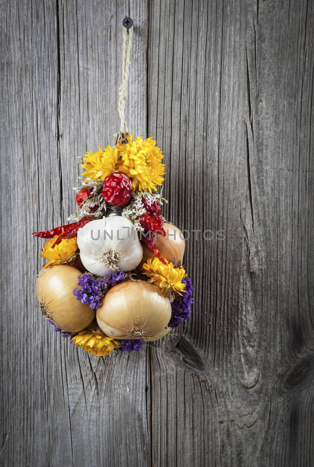 Braided bunch with onions, garlic and flowers, on wooden background