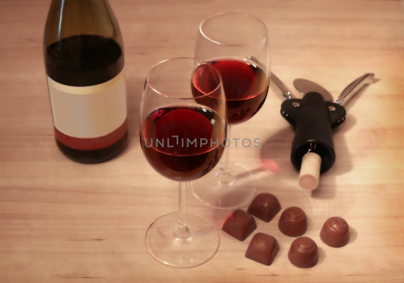 Two glasses of wine, bottle corkscrew and chocolate on table