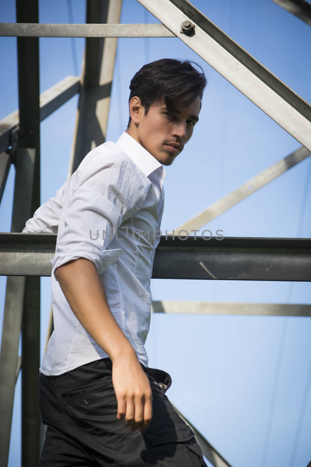 Handsome young man hanging from metal electricity trellis, looking at camera