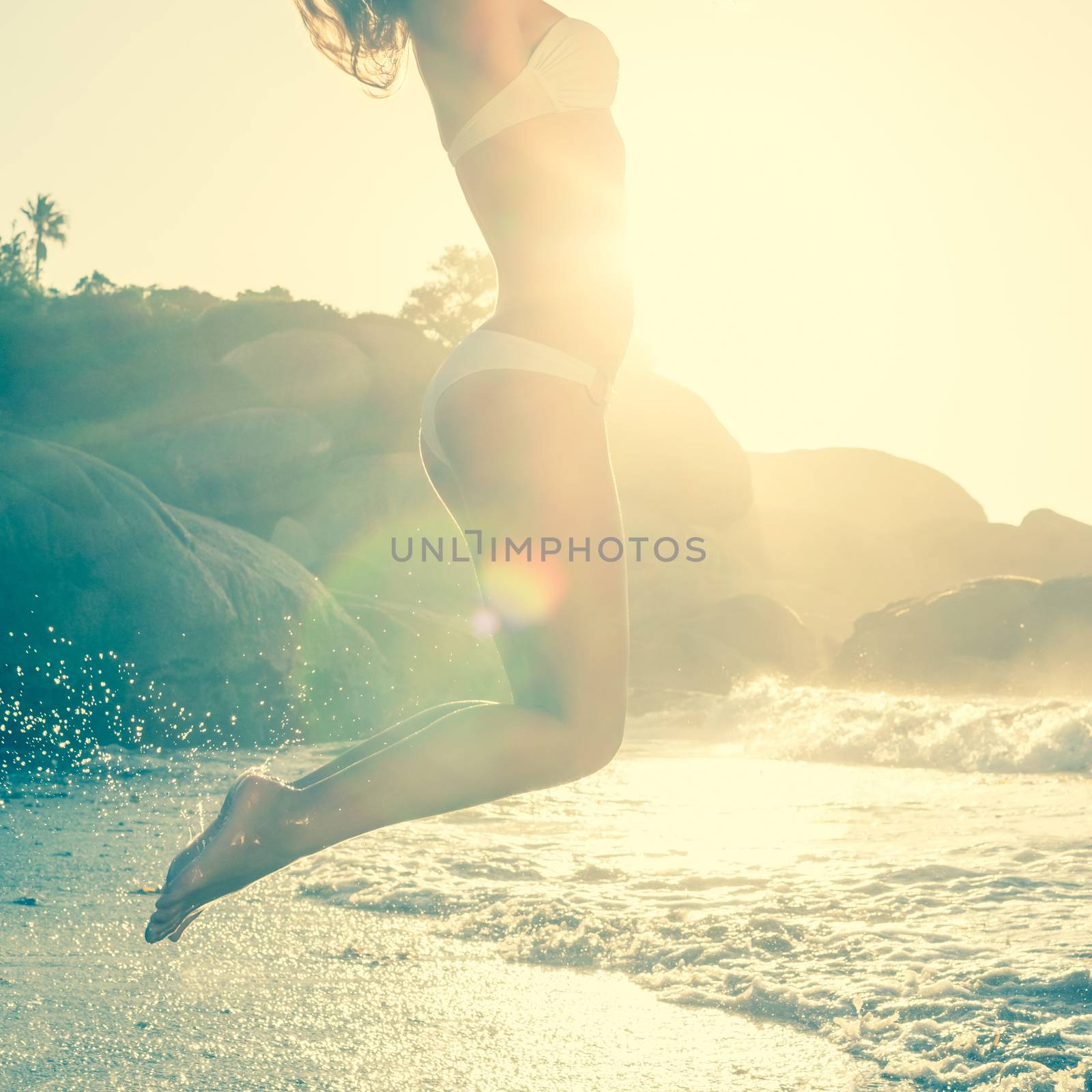 Beautiful jumping blonde in white bikini at the beach by Wavebreakmedia