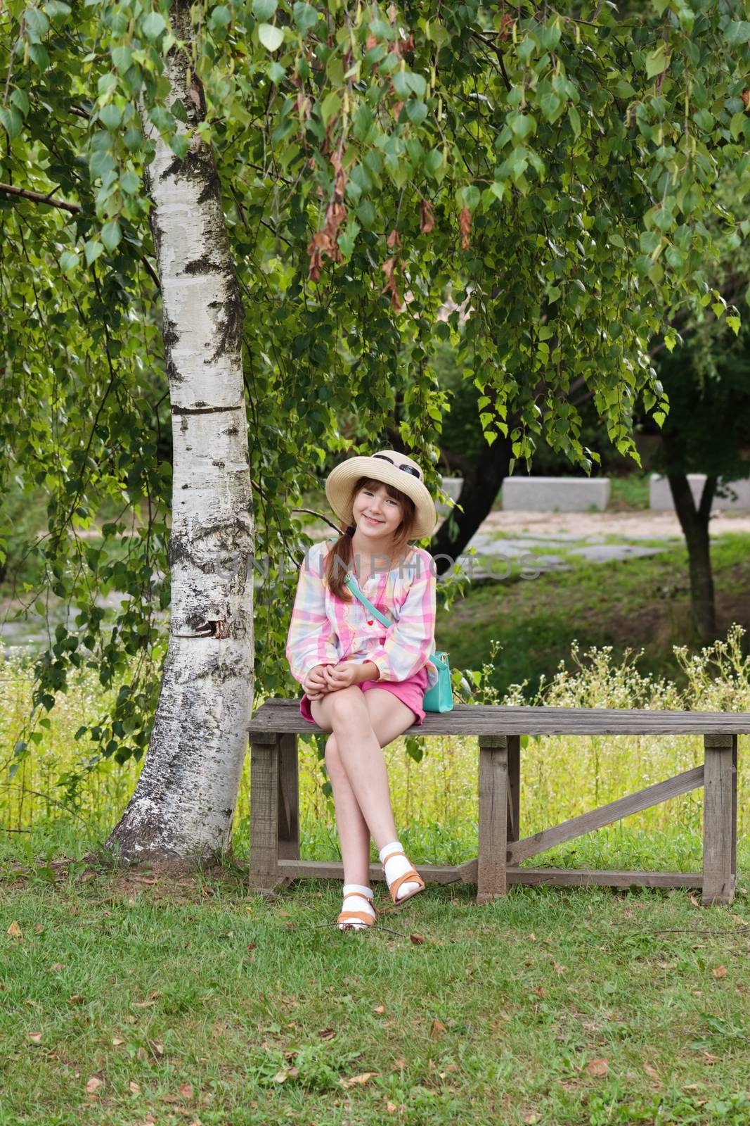 Happy girl sitting on the bench near the birch tree by dsmsoft