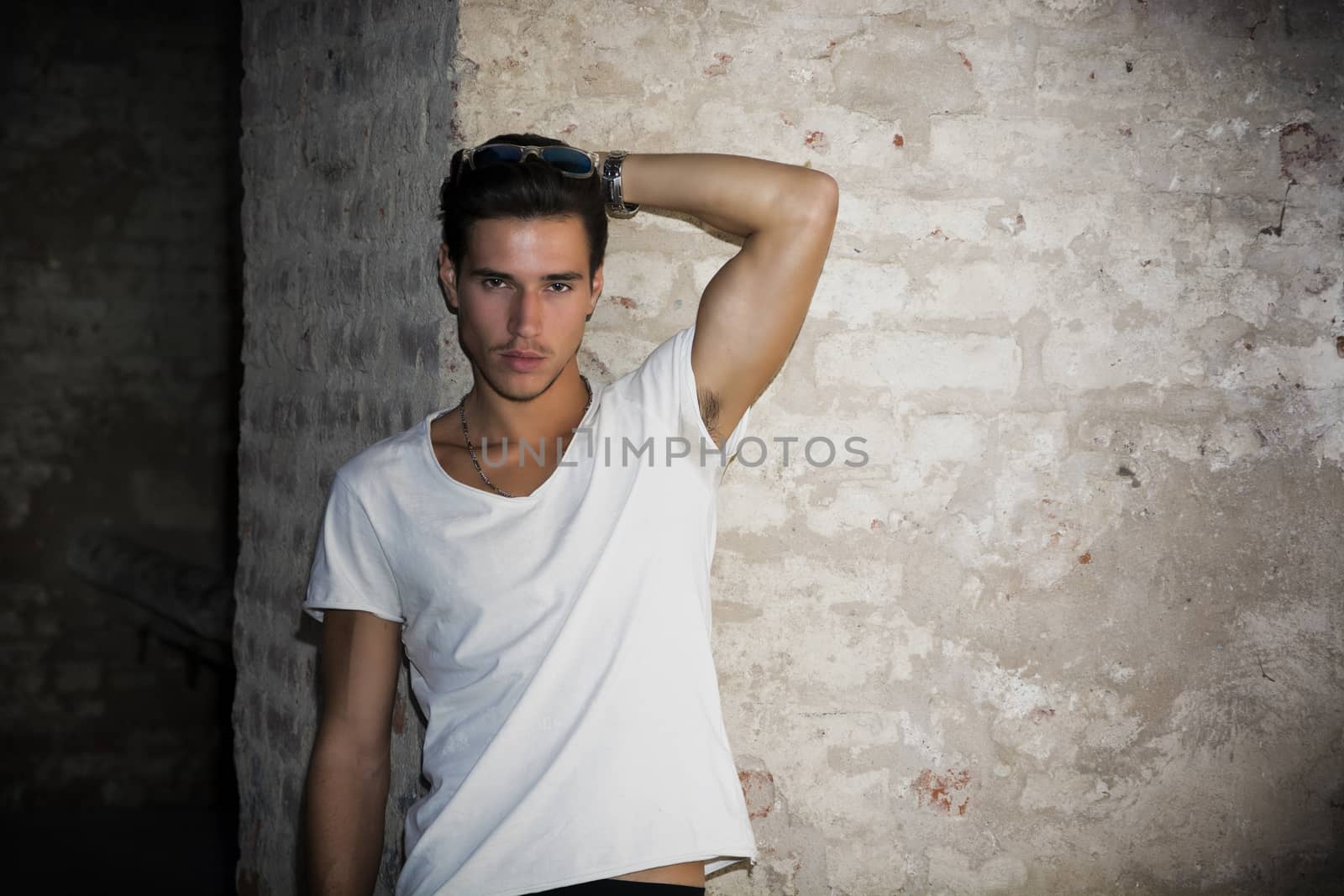 Handsome young man in old building against brick wall, looking at camera
