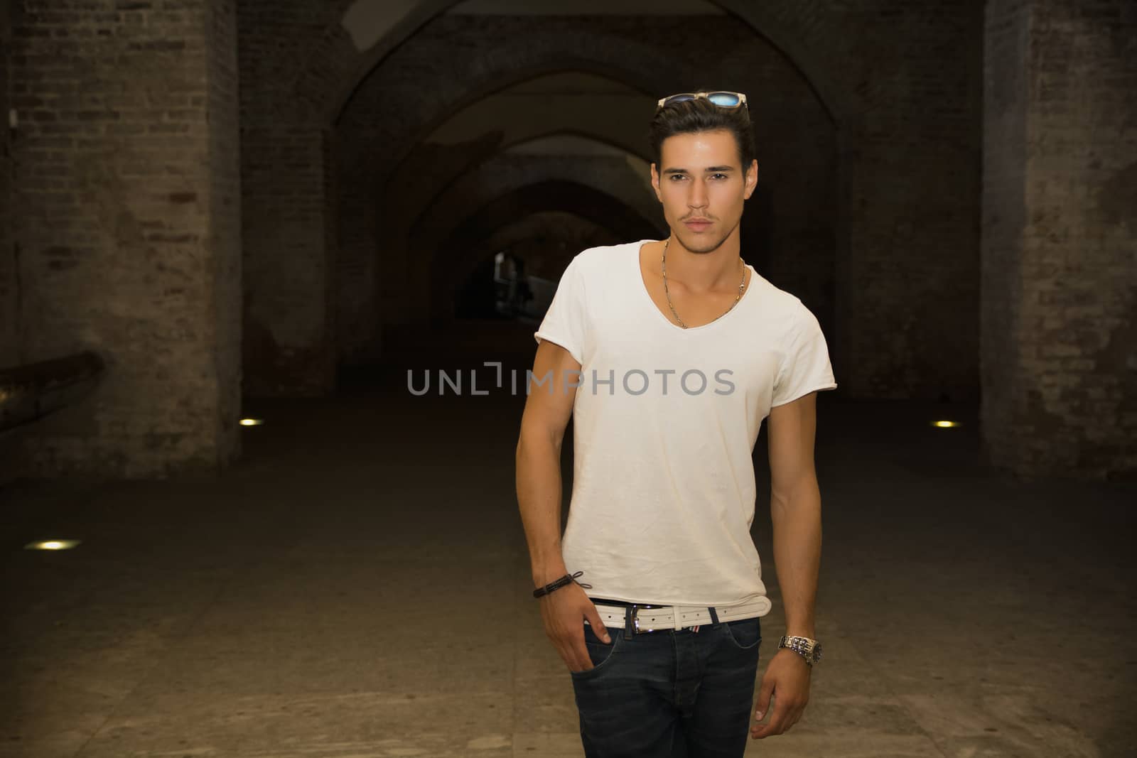 Handsome young man in old building walking inside gallery, looking at camera