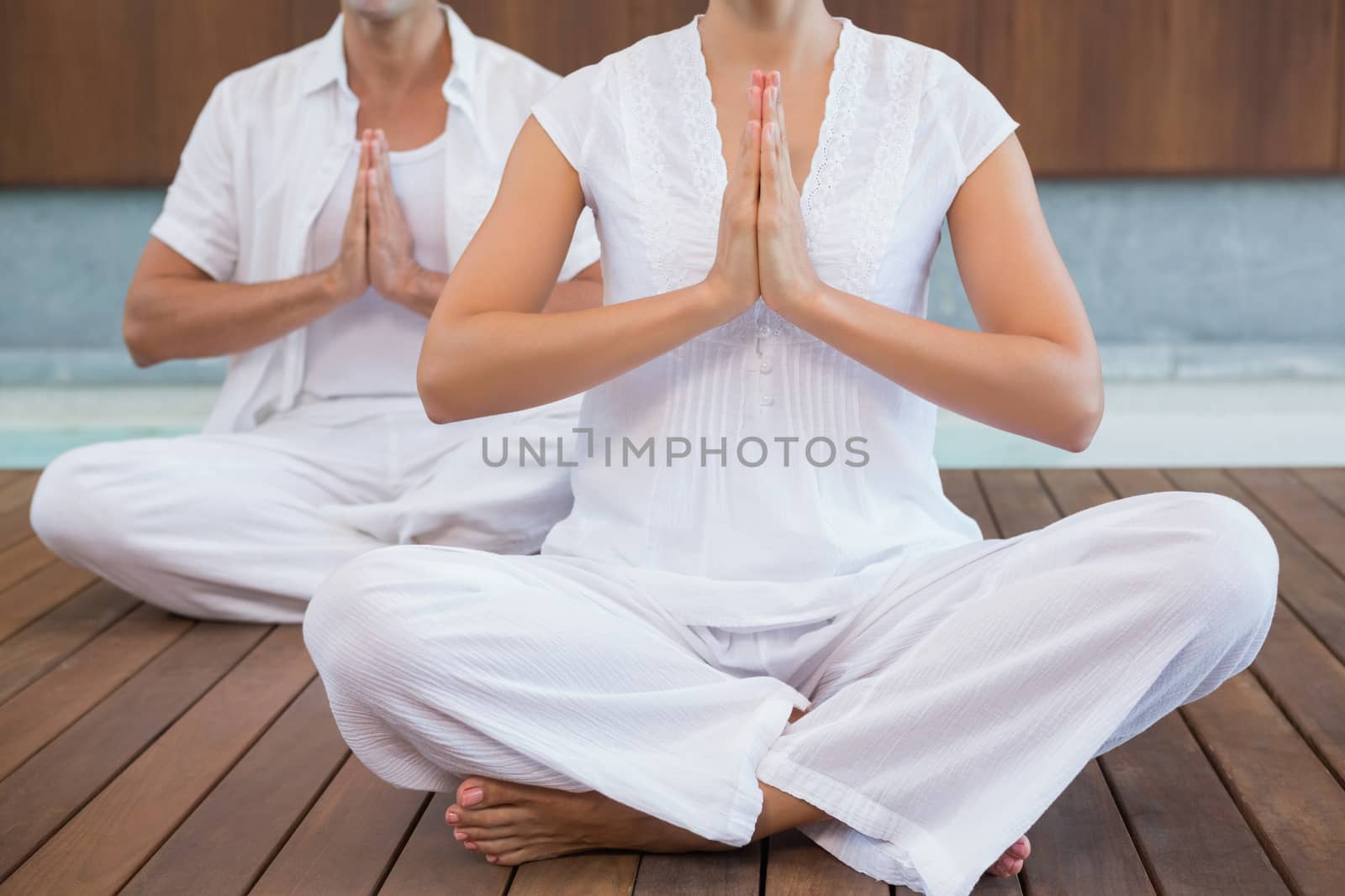 Couple in white sitting in lotus pose with hands together by Wavebreakmedia