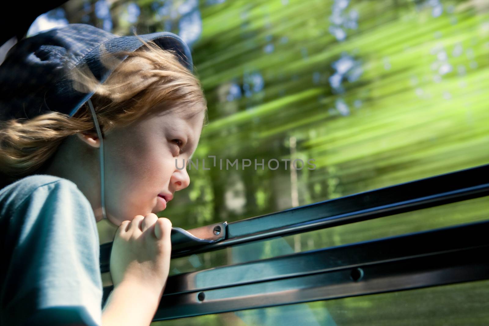 boy with long blond hair and hat looking out the train window