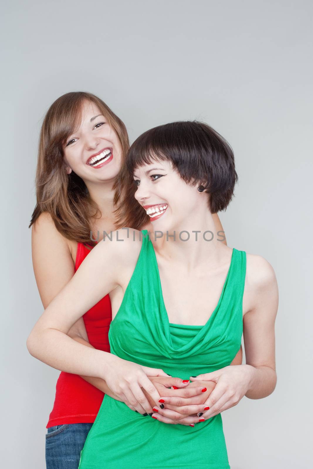 two happy young women standing, smiling - isolated on gray