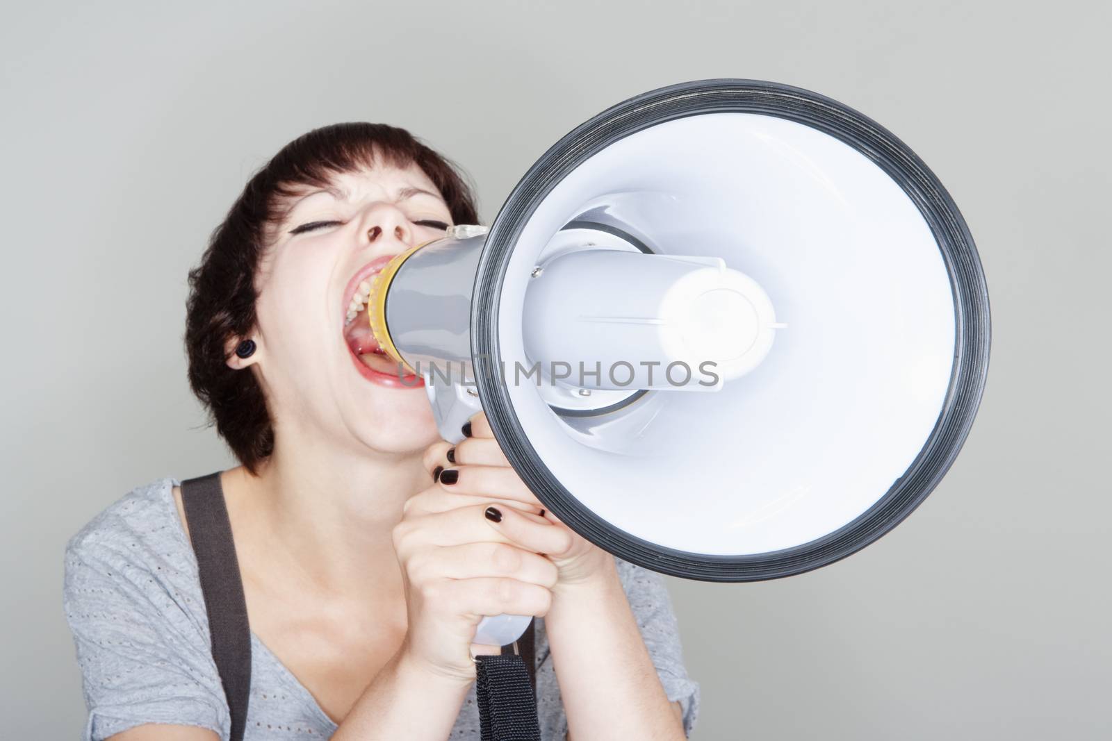 angry teenage girl yelling into a megaphone - isolated on gray