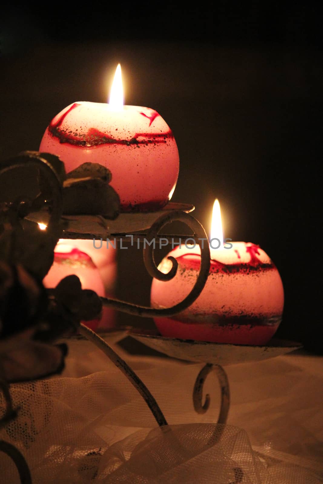 A curved metal candle holder set on a table covered with netting. Soft pink light is emitted from the lit candles.