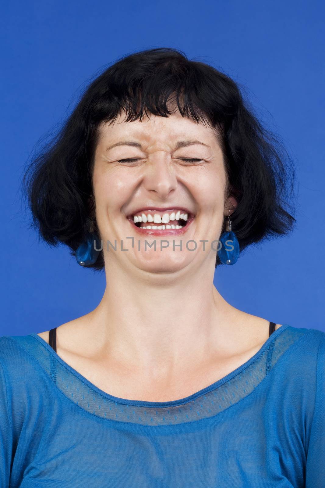 portrait of middle-aged woman with dark hair laughing - isolated on blue