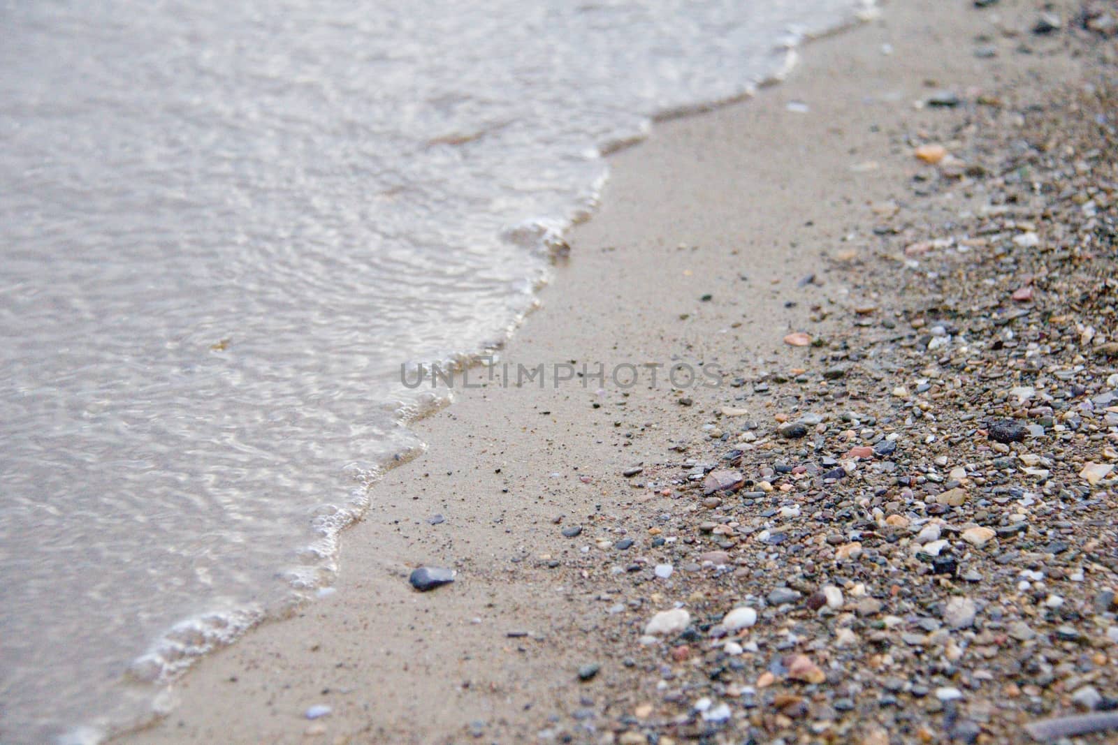 Photo shows a detail of the various stones on the sandy beach.