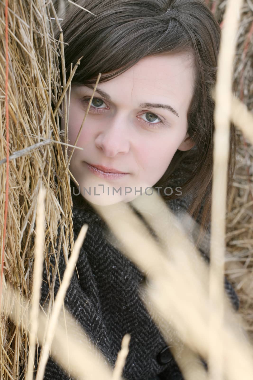 Beautiful brunette female sitting against a hay bale 