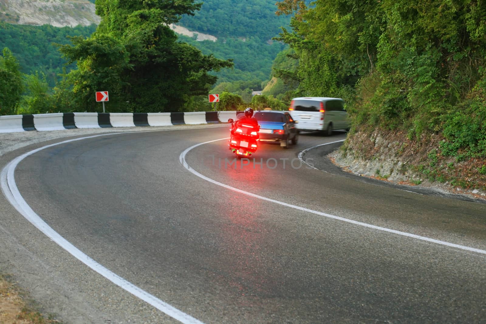 Cars and motorcycle driving on twisting road to mountains