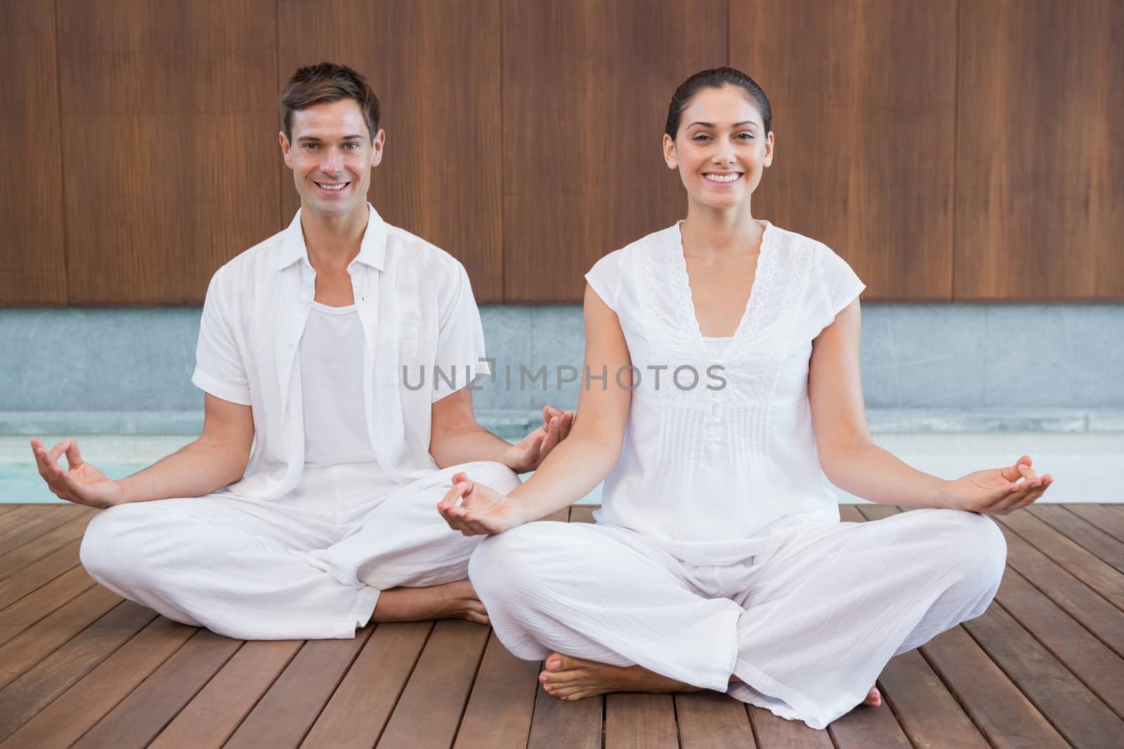 Attractive couple in white sitting in lotus pose smiling at camera by Wavebreakmedia